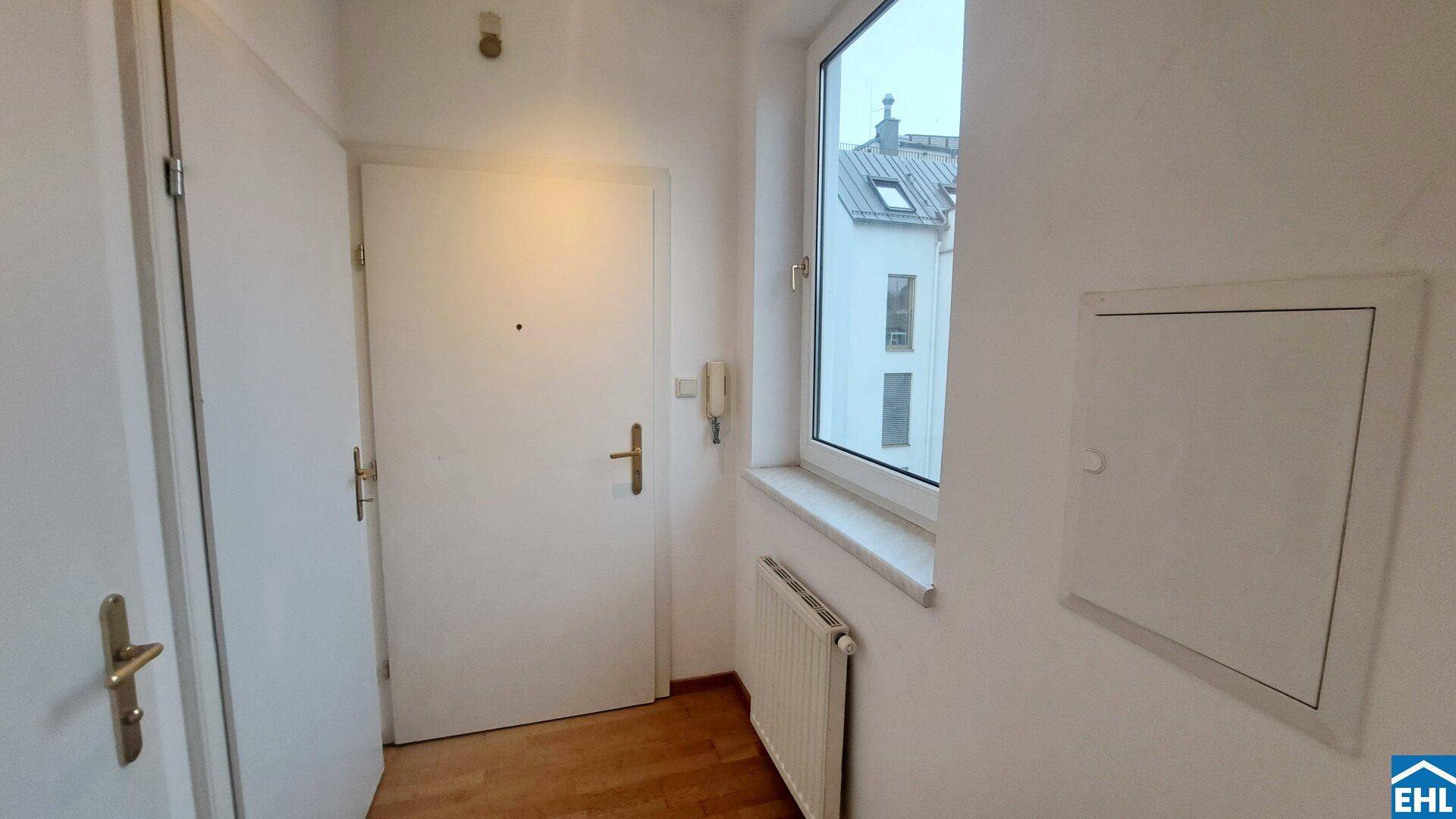 Heller Eingangsbereich mit Fenster, Heizkörper und Zugang zur Wohnung.