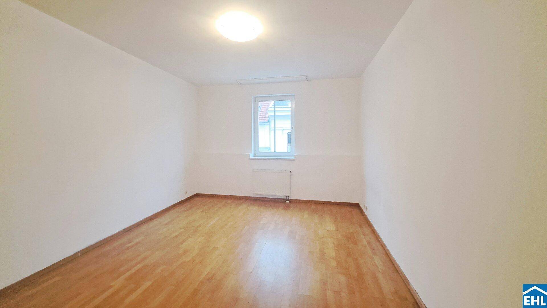 Helles, leeres Zimmer mit weißen Wänden und klassischem Parkettboden, bereit zur individuellen Gestaltung.