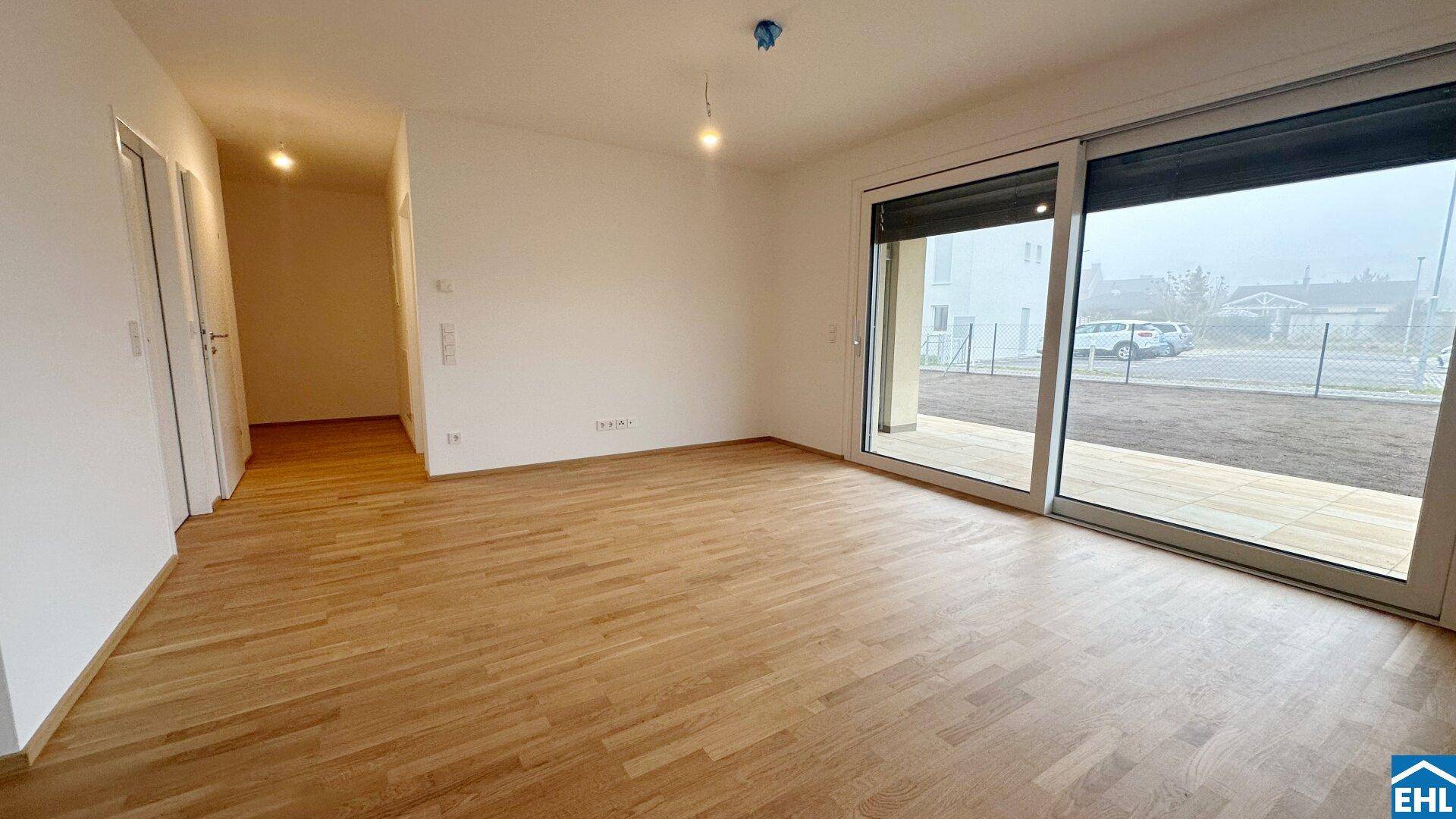 Geräumiges Wohnzimmer mit Holzboden und großen Schiebetüren, die Zugang zur Terrasse bieten.