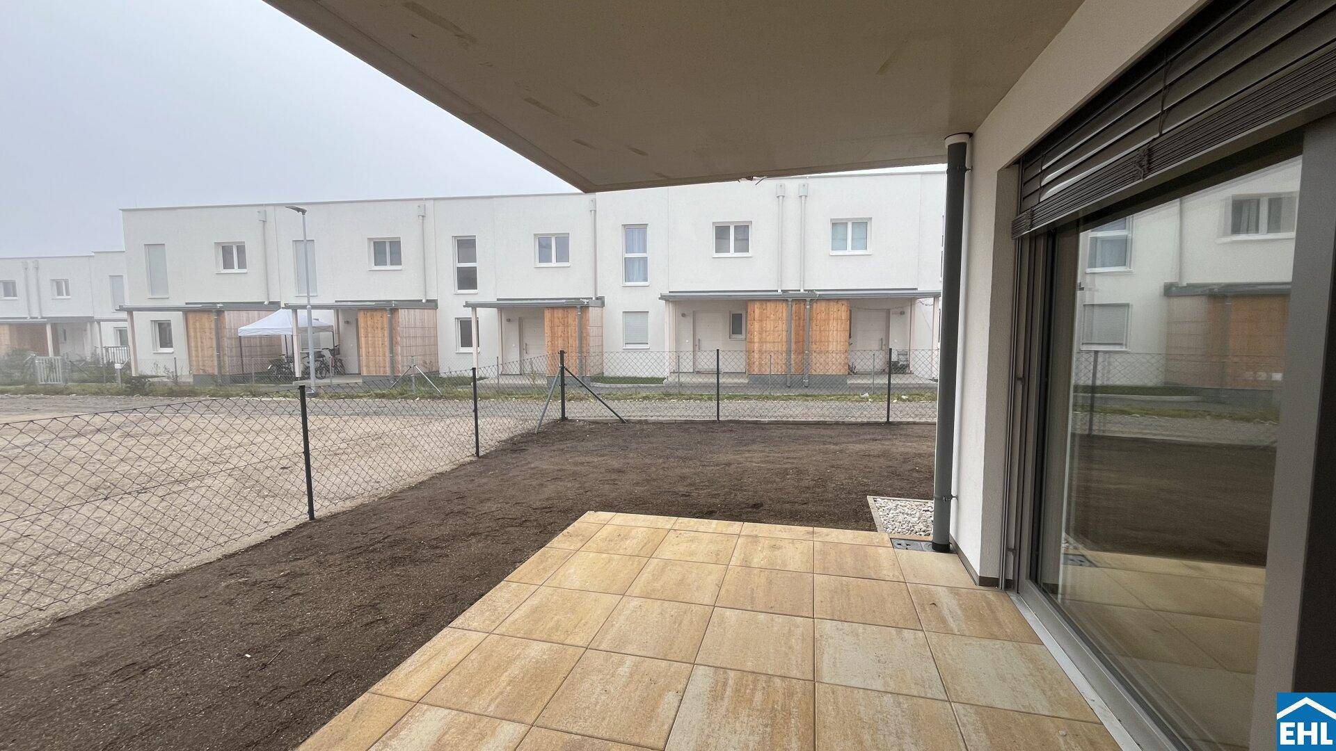 Gepflasterte Terrasse mit Blick auf die umliegenden Neubauten und einen kleinen Gartenbereich.