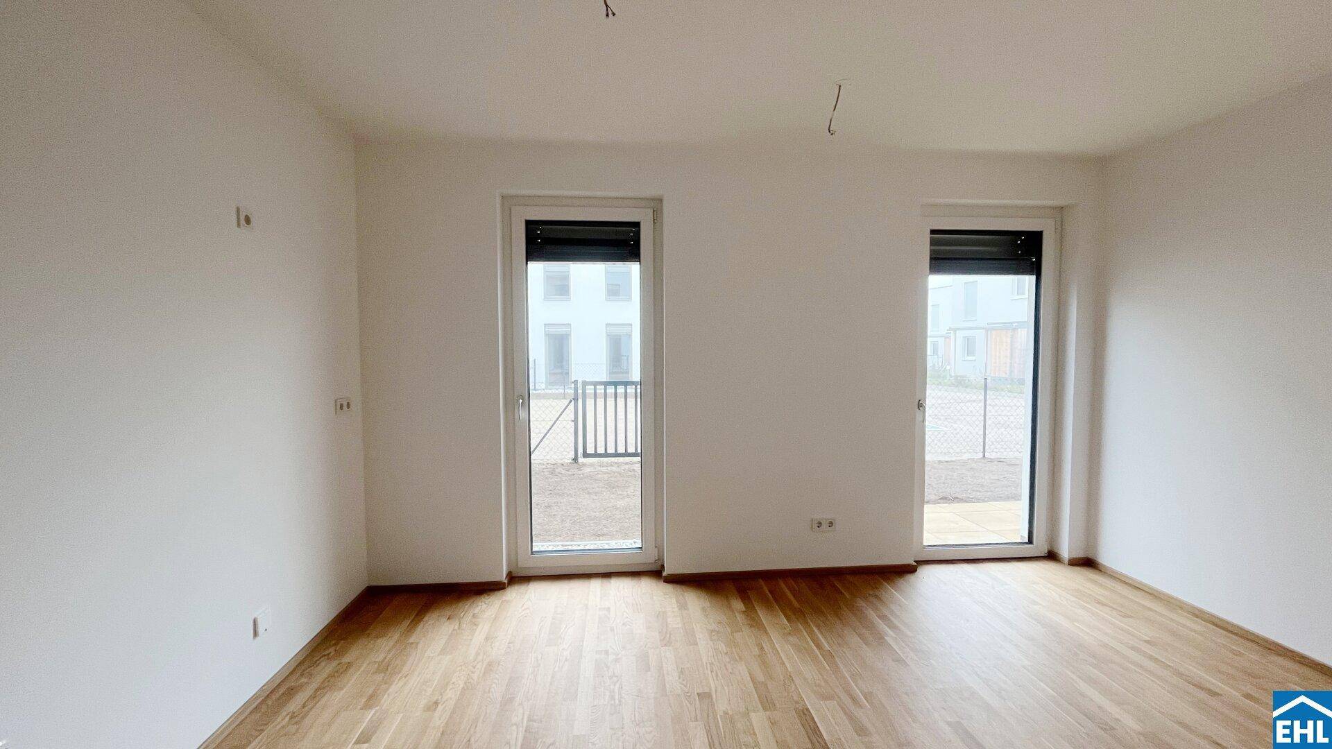 Lichtdurchfluteter Raum mit zwei Fenstertüren, eine davon mit französischem Balkon.