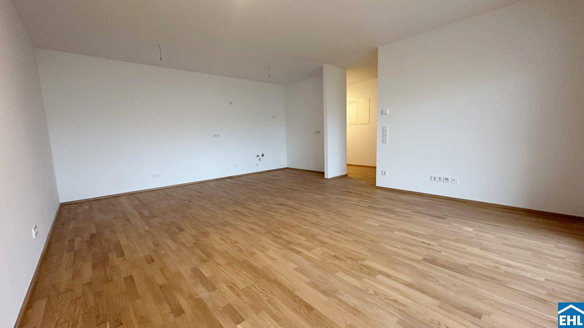 Geräumiger, leerer Wohnbereich mit hellem Holzparkett und weißen Wänden, bereit zur Einrichtung.