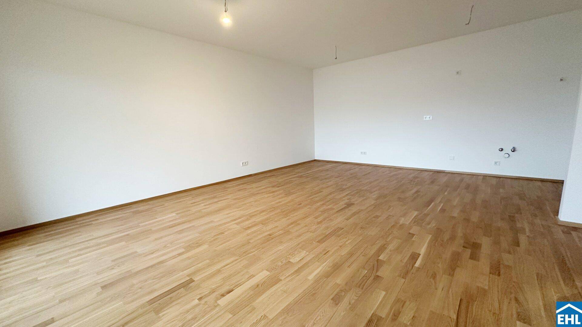 Großer, heller Raum mit Holzparkettboden und weißen Wänden, ideal für einen Wohnbereich.