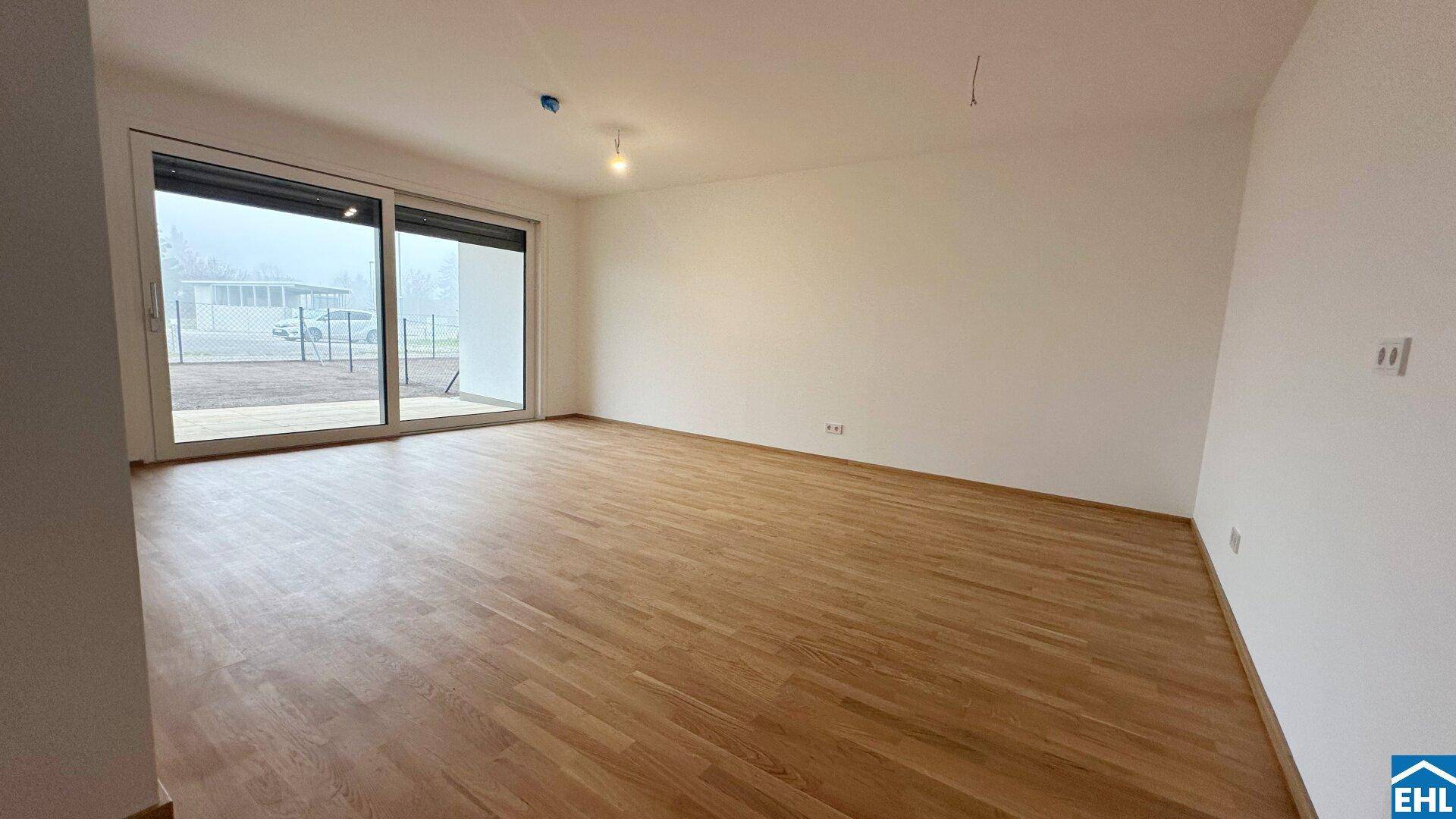 Heller Wohnbereich mit Holzparkett und großer Schiebetür, die Zugang zum Außenbereich bietet.