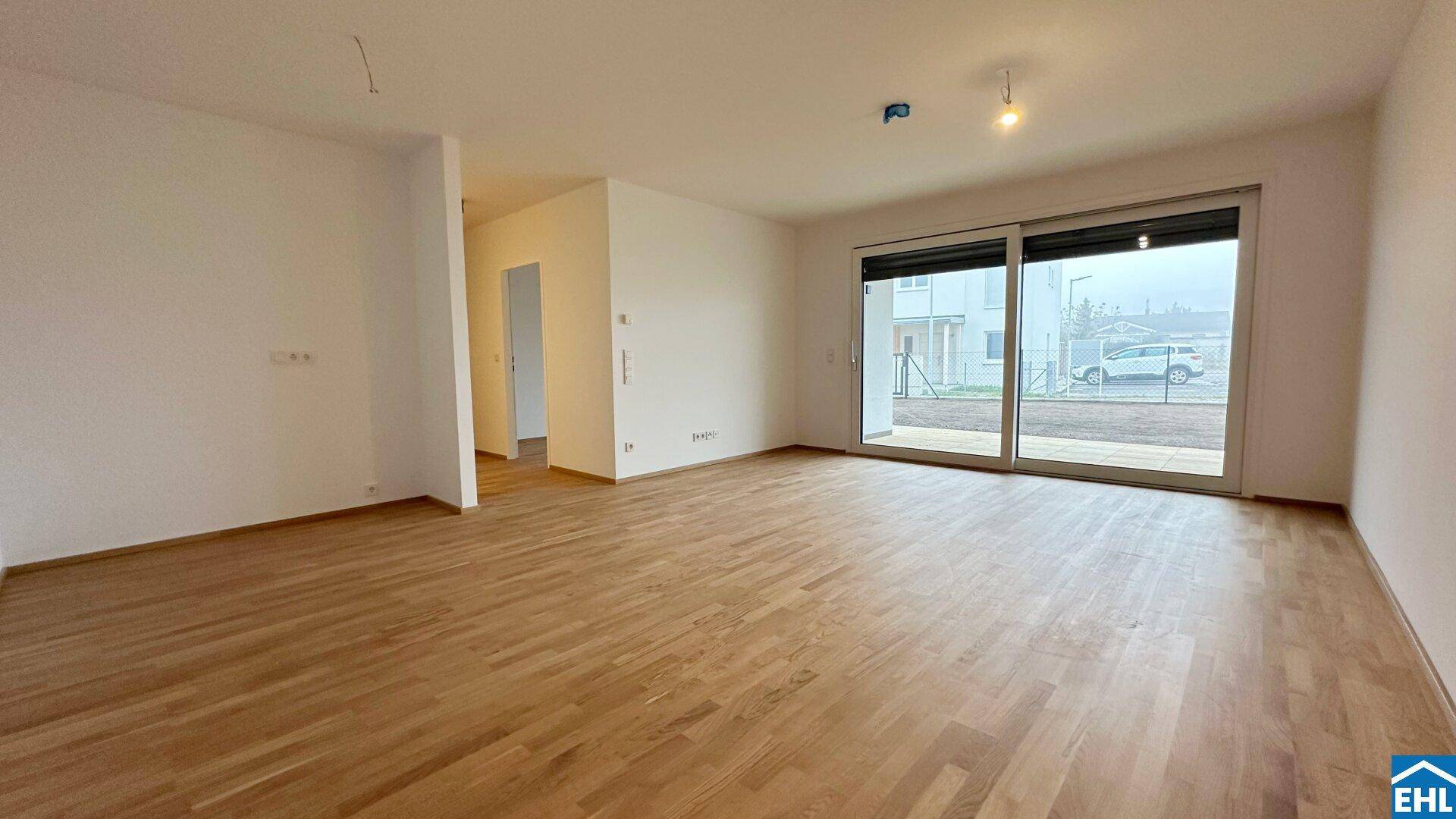 Geräumiger Wohnbereich mit Holzparkett und breiter Schiebetür, die viel Tageslicht hereinlässt.