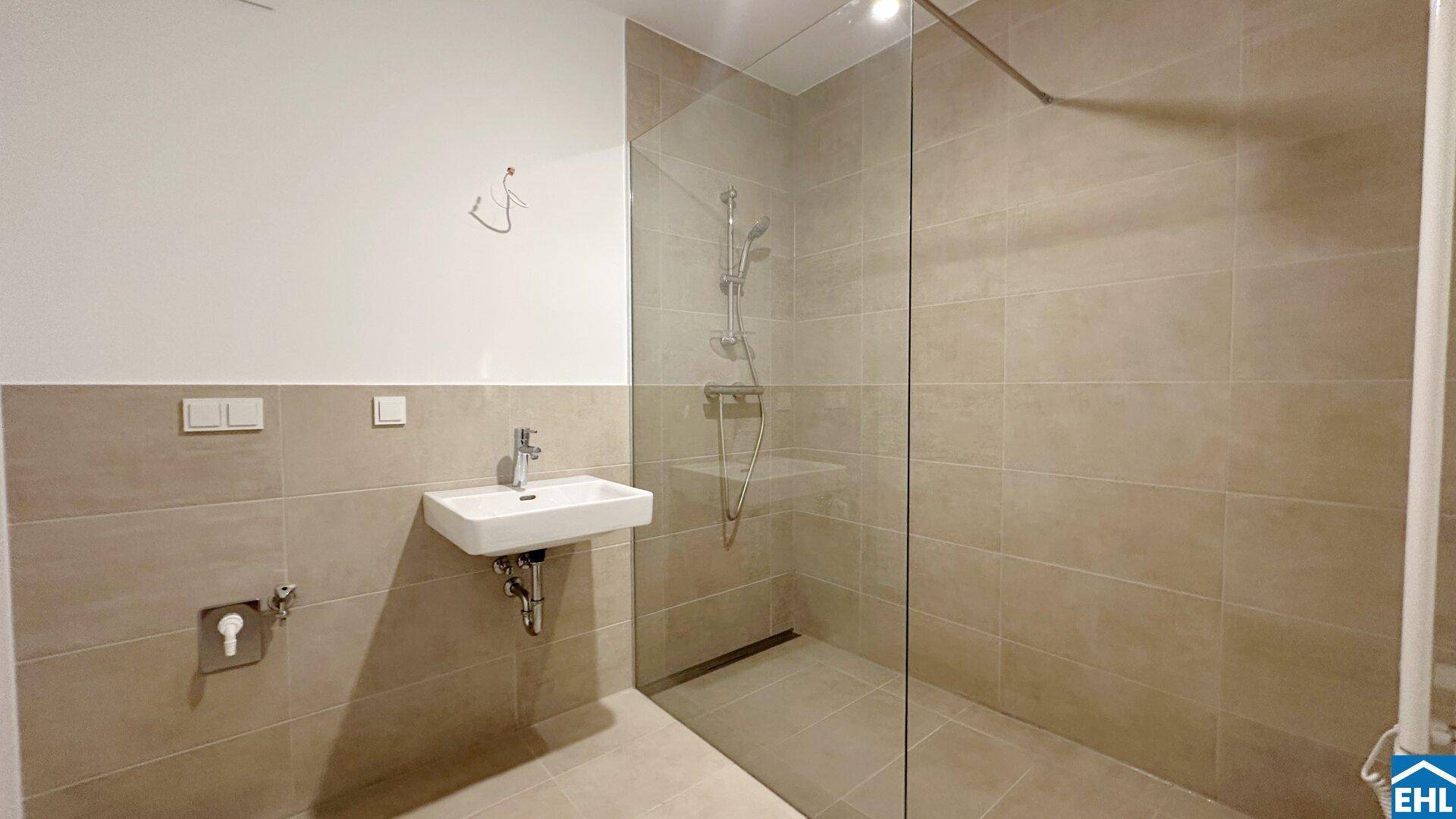 Modernes Badezimmer mit beigefarbenen Fliesen, ebenerdiger Dusche und minimalistischem Waschbecken.