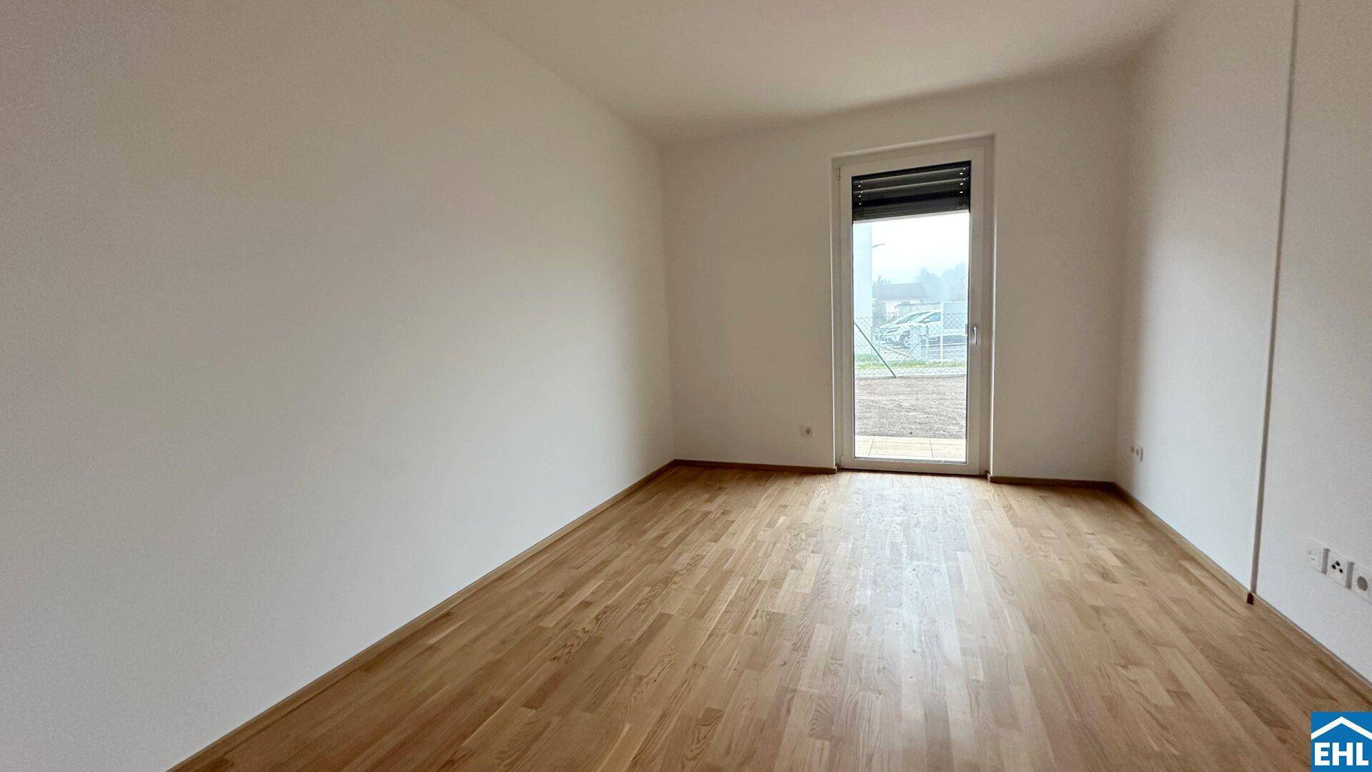 Helles Schlafzimmer mit Holzparkettboden und Zugang zu einem Außenbereich durch eine Glastür.