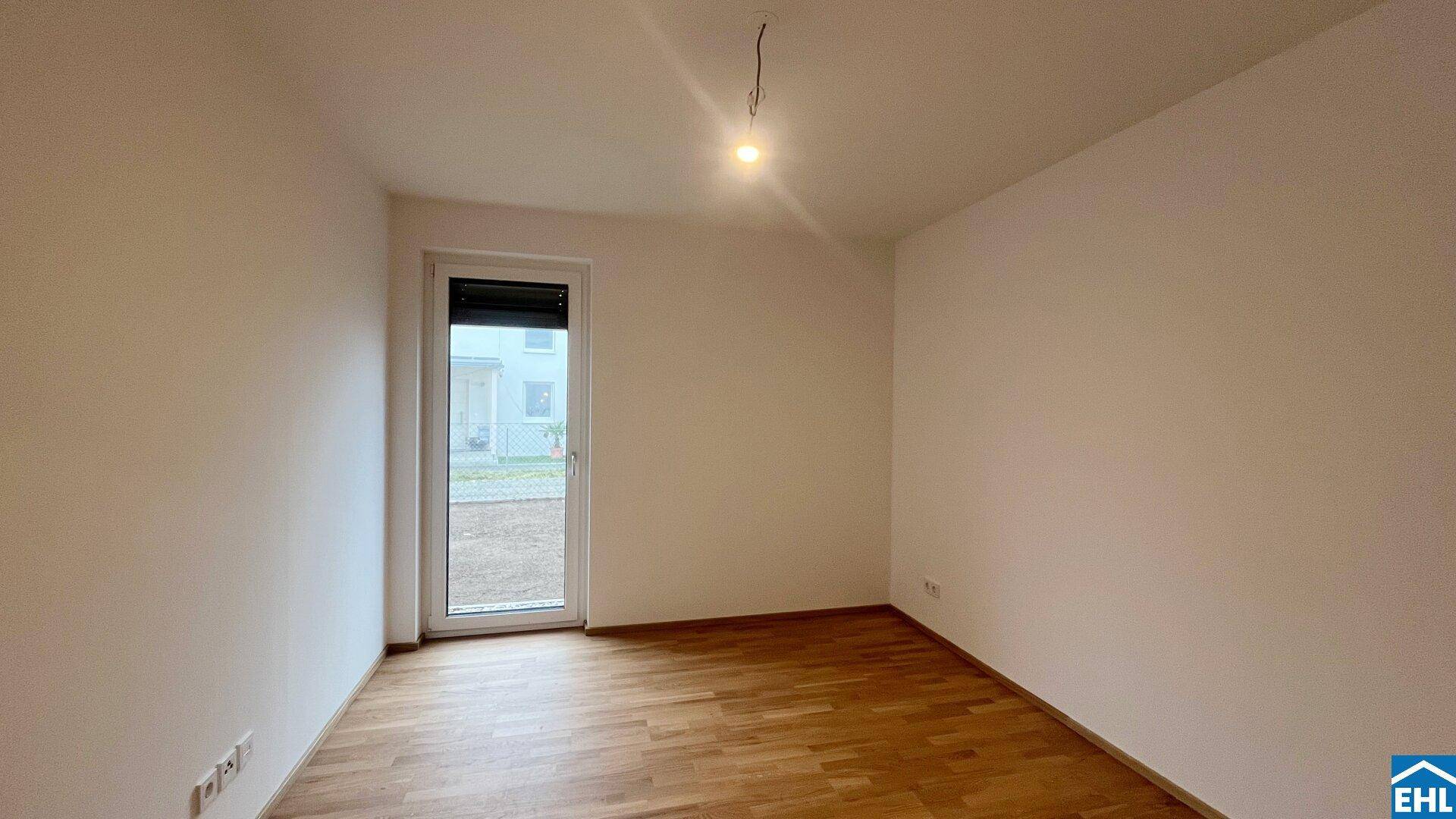 Leeres Schlafzimmer mit Holzboden und Fenstertür zum Außenbereich.