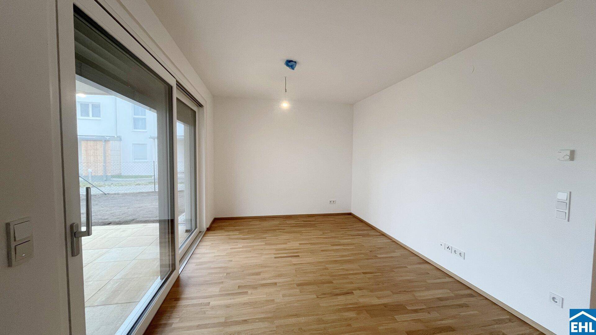 Geräumiges, leeres Wohnzimmer mit Holzboden und großen Schiebetüren zum Außenbereich.