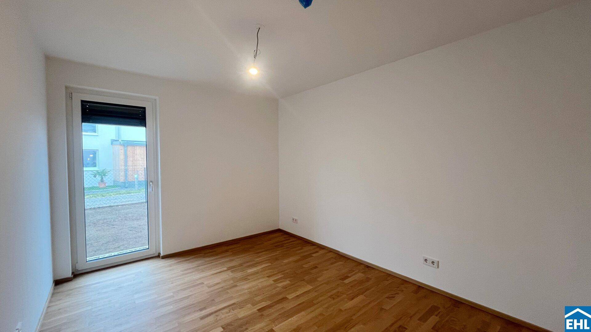 Heller, leerer Raum mit Holzboden und Fenstertür, die ins Freie führt.