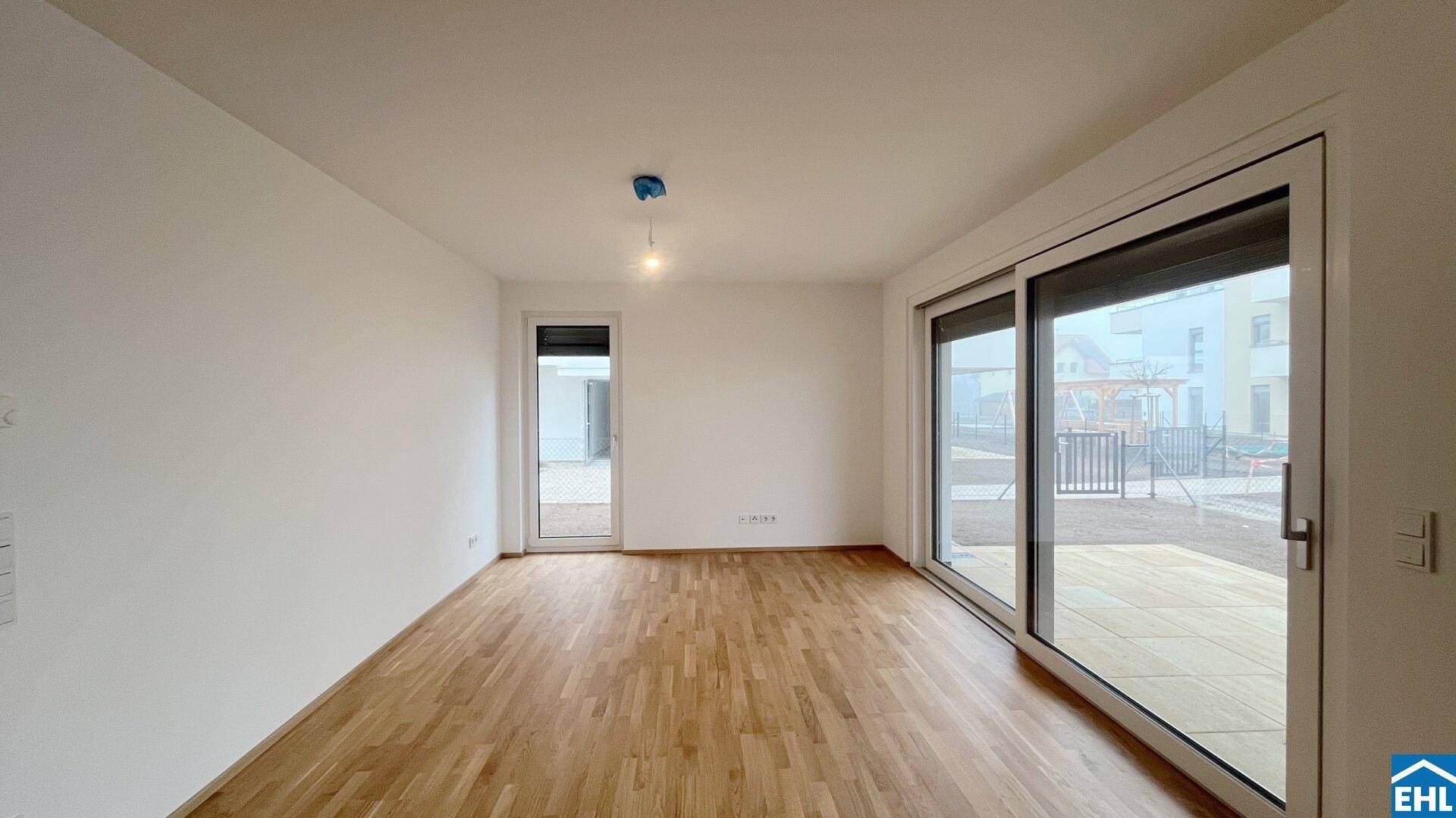 Geräumiger, unmöblierter Wohnbereich mit hellem Parkettboden und großen Schiebetüren zur Terrasse.