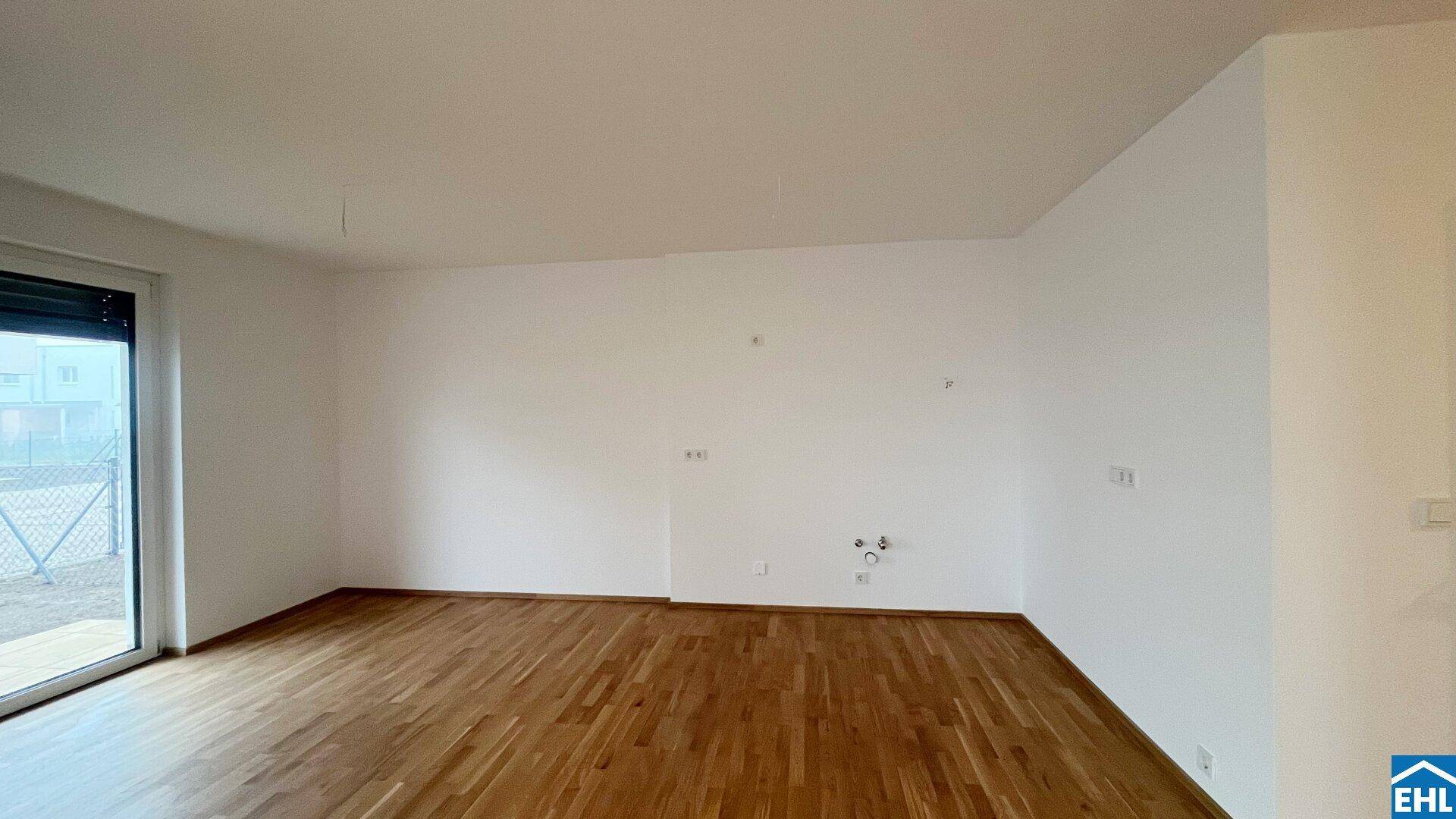 Unmöblierter Raum mit Holzboden und Anschlüssen an der Wand, bereit für die Kücheninstallation.