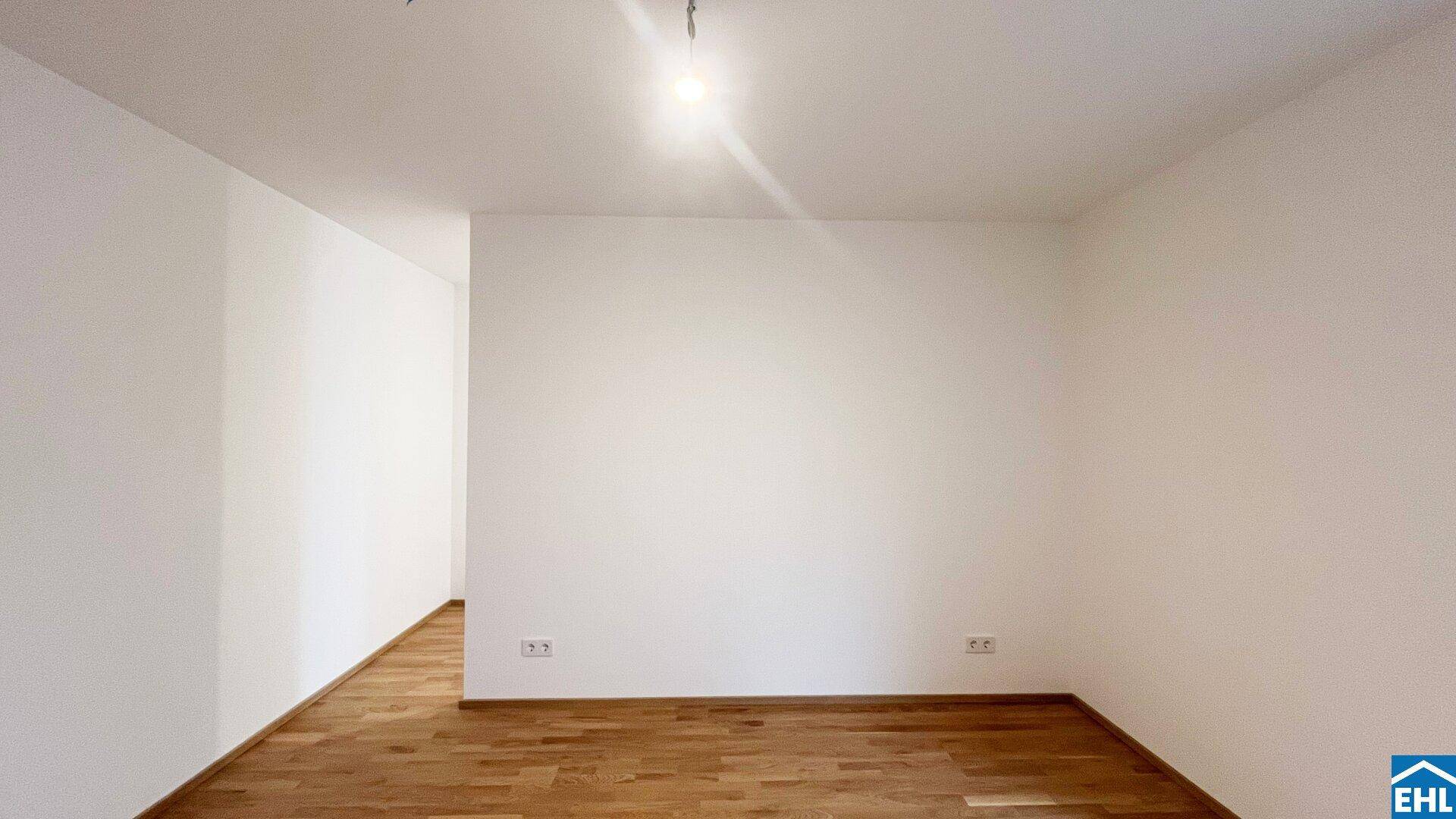 Heller Flur mit Holzboden und weißen Wänden, der zu weiteren Räumen führt.