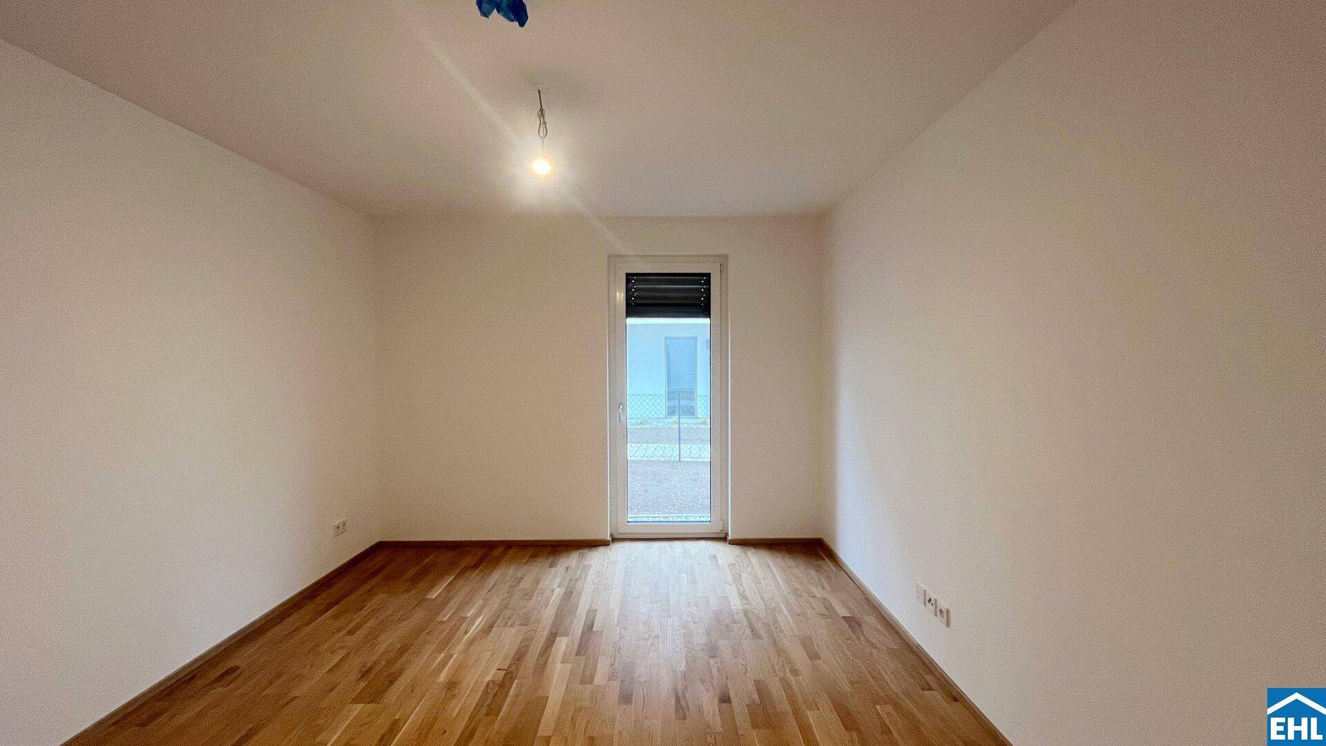 Helles, unmöbliertes Zimmer mit Holzboden und Zugang zu einem Außenbereich.