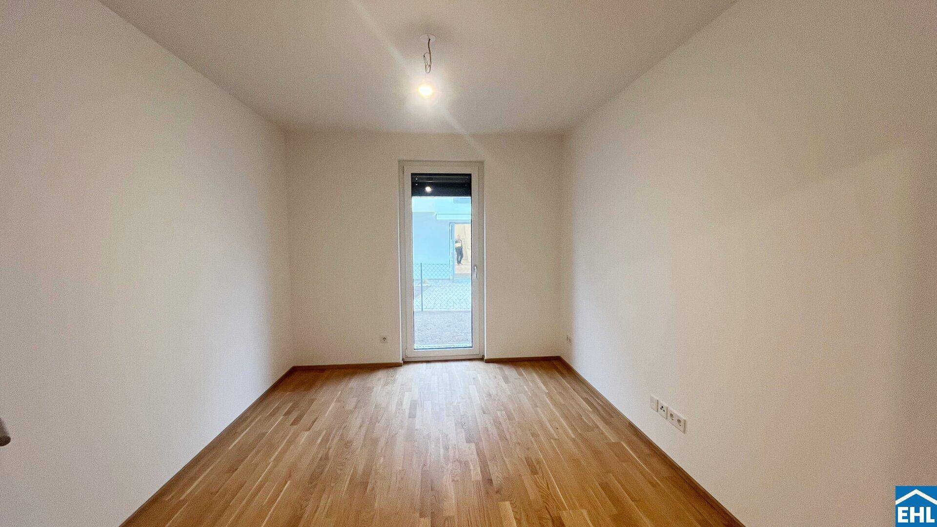 Leeres Zimmer mit Holzboden und einer Tür, die zu einem Außenbereich führt.
