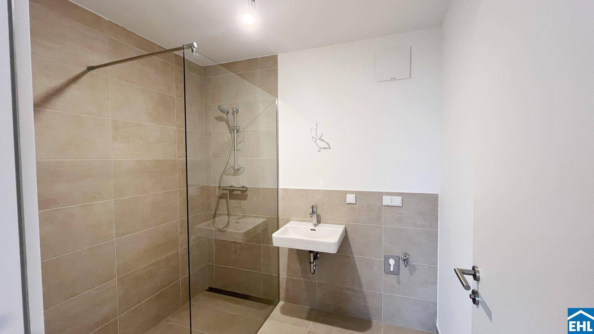 Modernes Badezimmer mit begehbarer Dusche, einzelnen Waschbecken und hellen Fliesen.