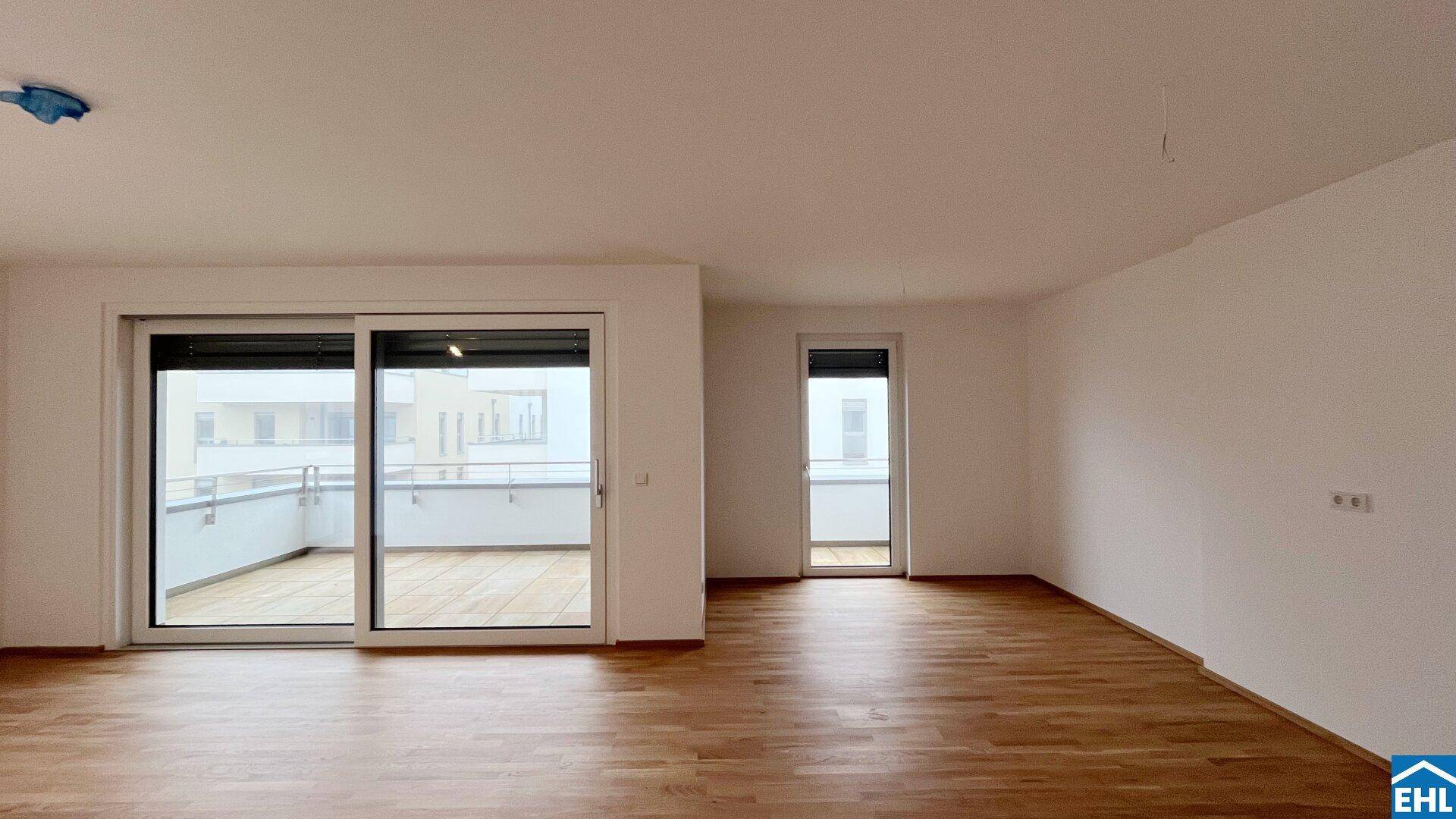 Großes, unmöbliertes Wohnzimmer mit Parkettboden und Zugang zu Balkon und Loggia.
