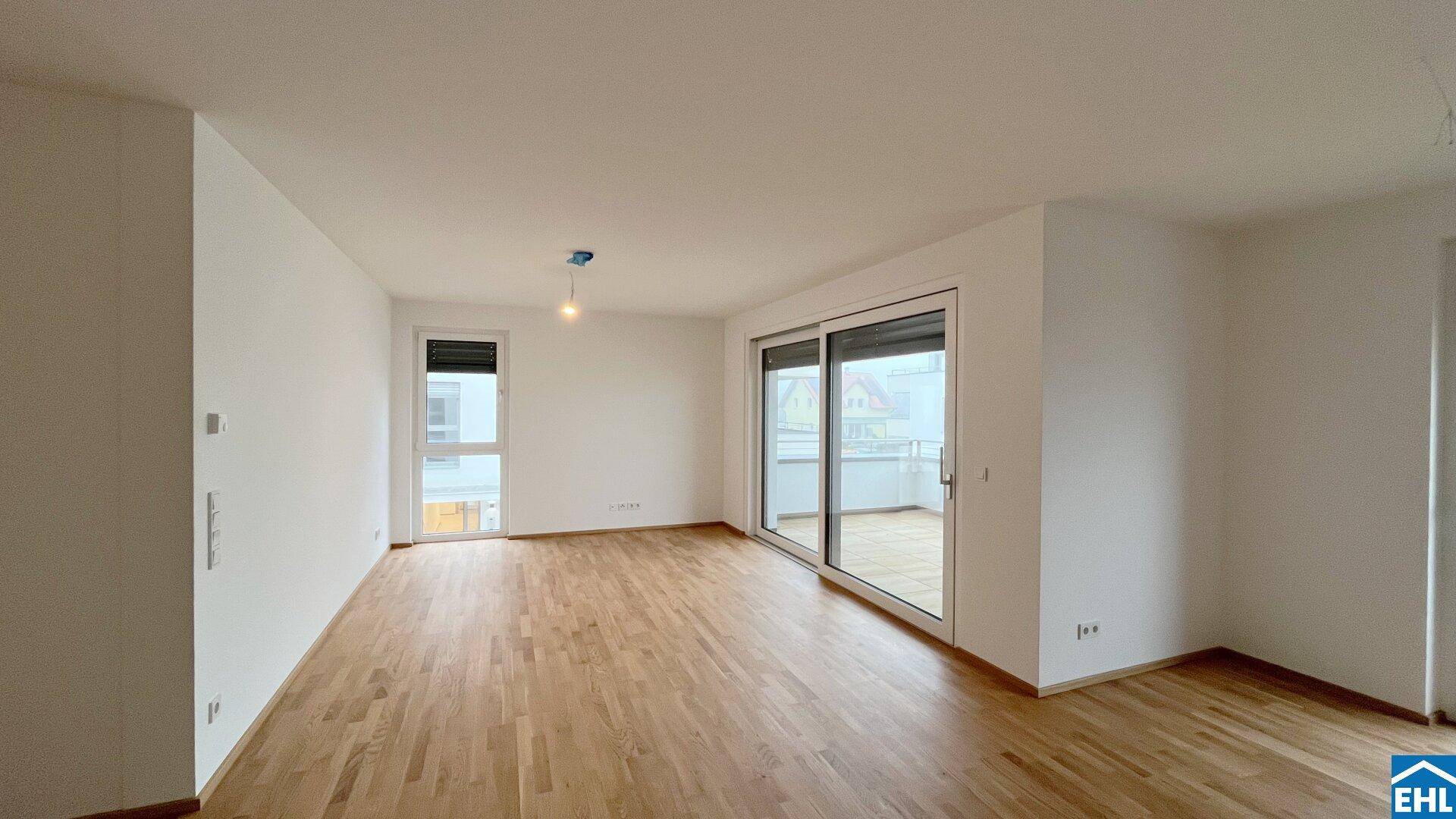 Helles Wohnzimmer mit Holzboden und breiter Schiebetür, die auf den Balkon führt.