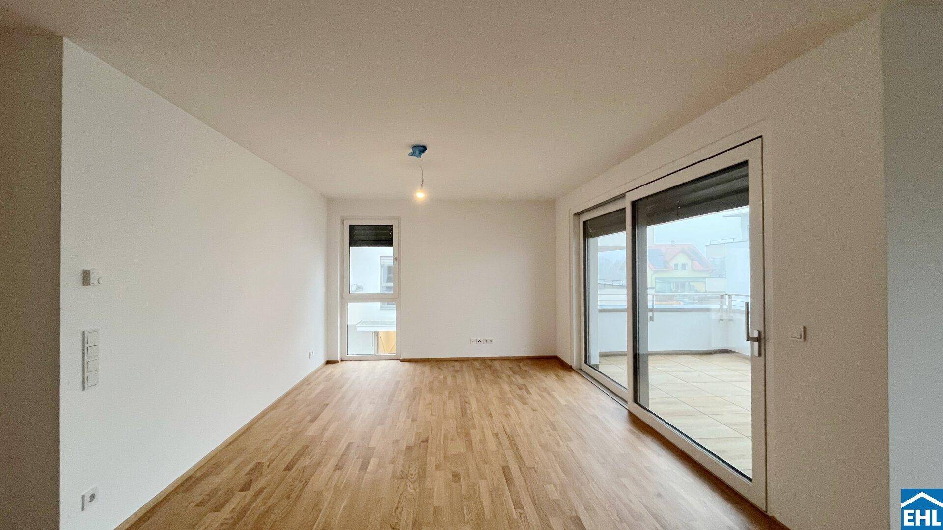 Geräumiges, unmöbliertes Wohnzimmer mit Parkettboden und großem Schiebefenster zum Balkon.