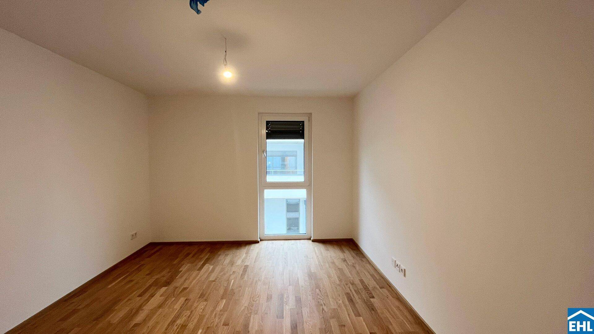 Leeres Zimmer mit hellem Parkettboden und Zugang zu einem französischen Balkon.
