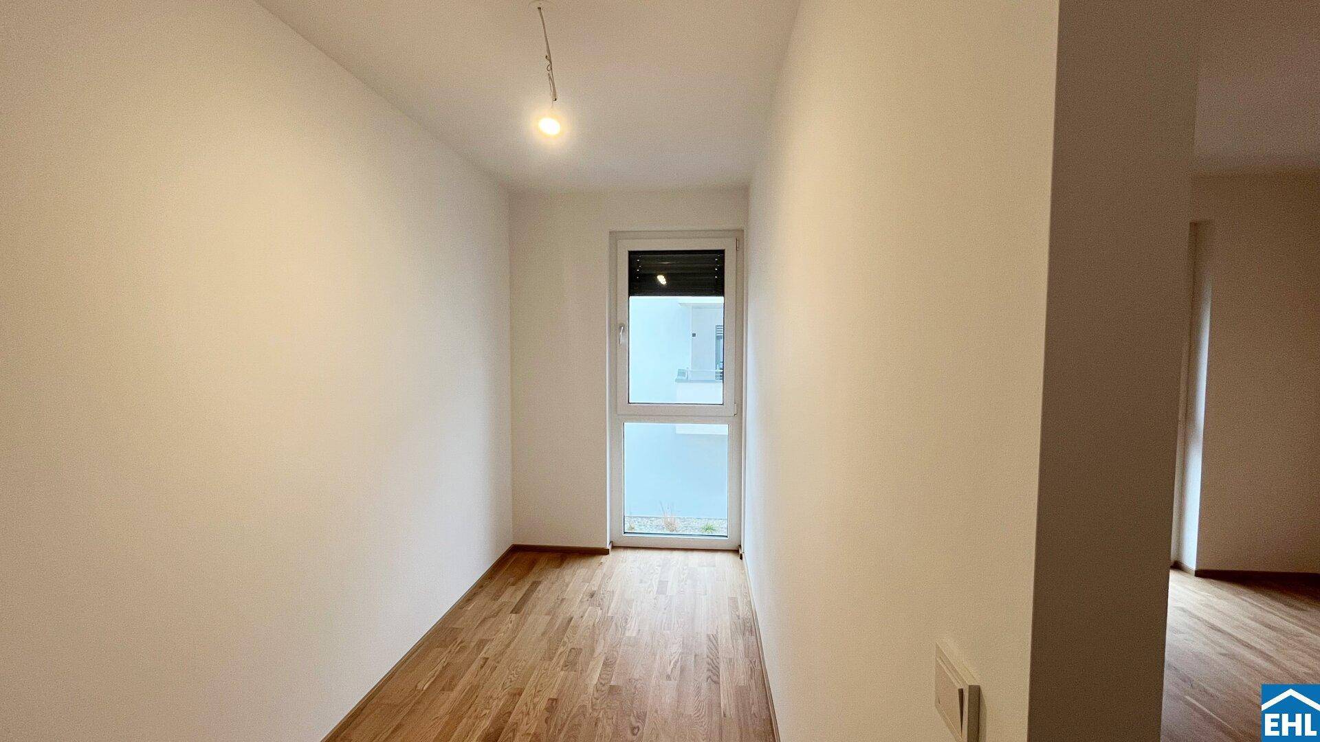 Unmöbliertes Zimmer mit Holzboden und Fenster, das viel Tageslicht hereinlässt.