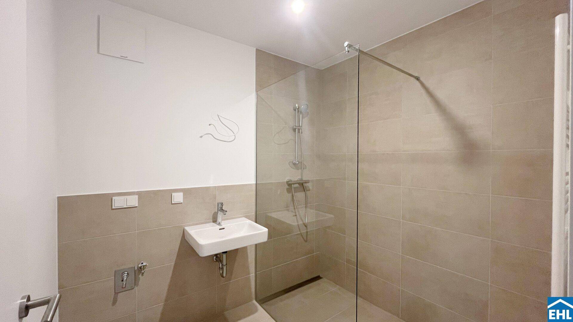 Modernes Badezimmer mit begehbarer Dusche, beigen Fliesen und minimalistischem Design.