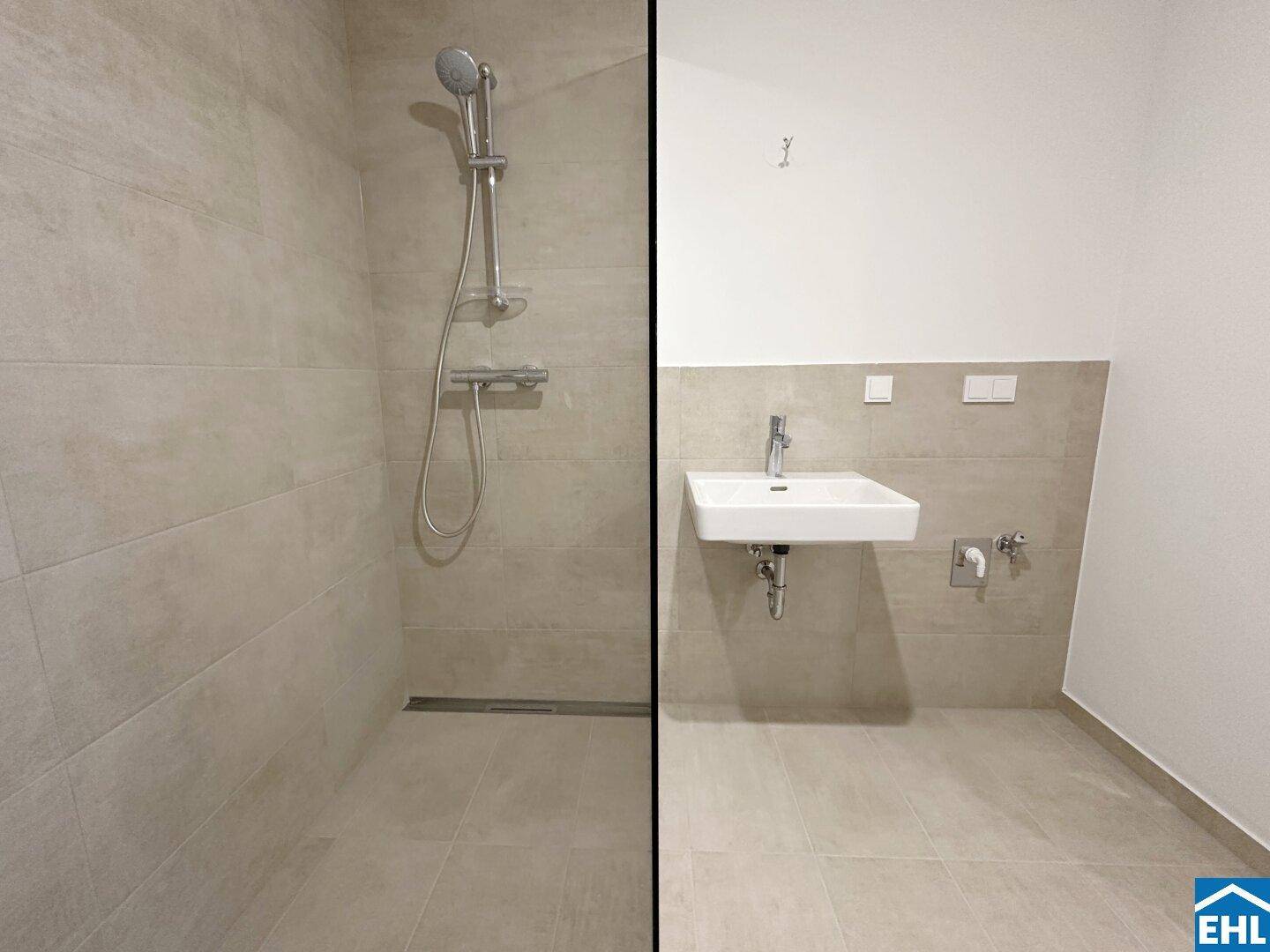 Modernes Badezimmer mit begehbarer Dusche und Waschbecken, ausgestattet mit hellen Fliesen.