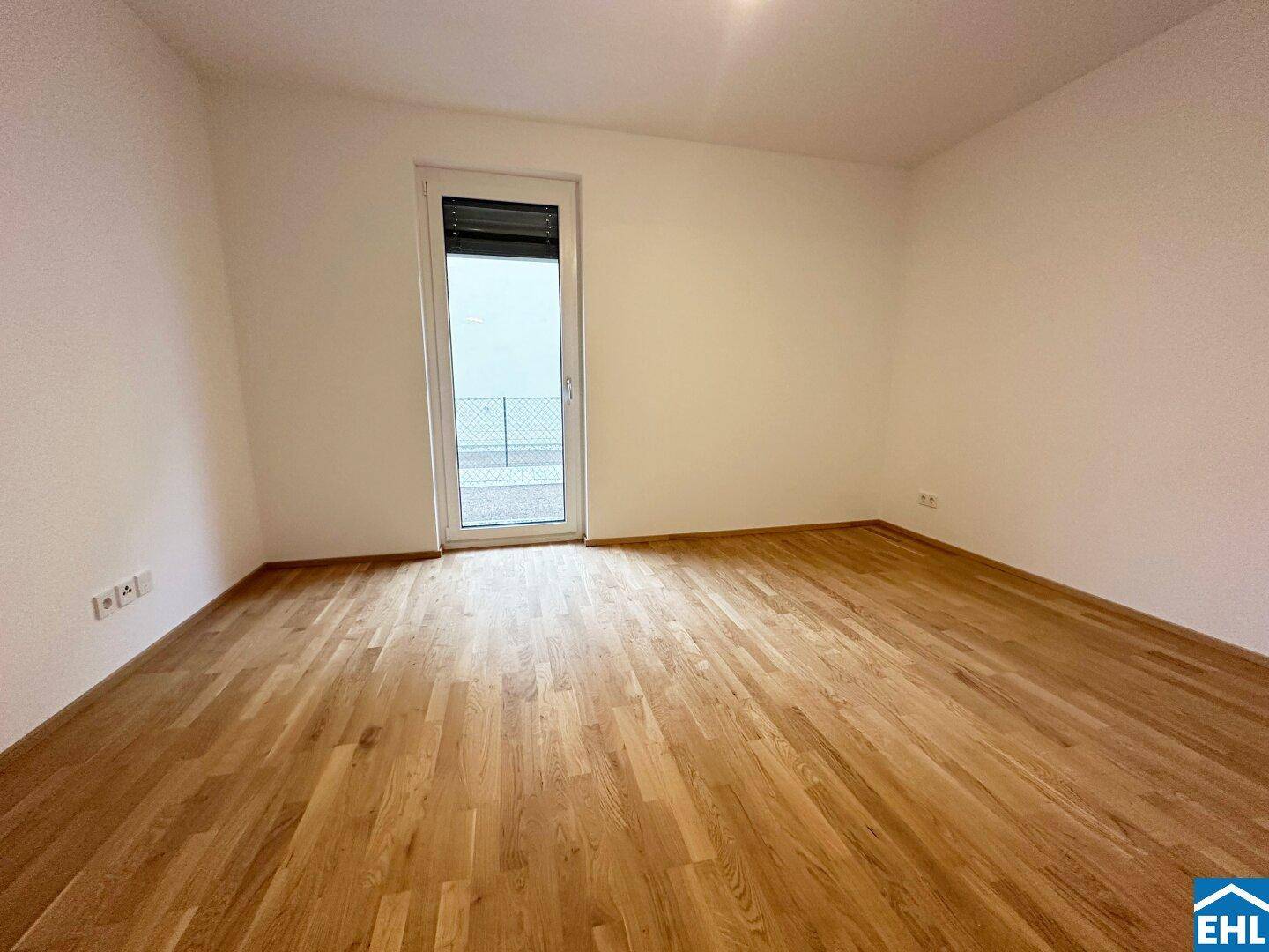 Leeres Schlafzimmer mit Holzboden und einer Tür, die zu einem Außenbereich führt, ideal für neue Bewohner.