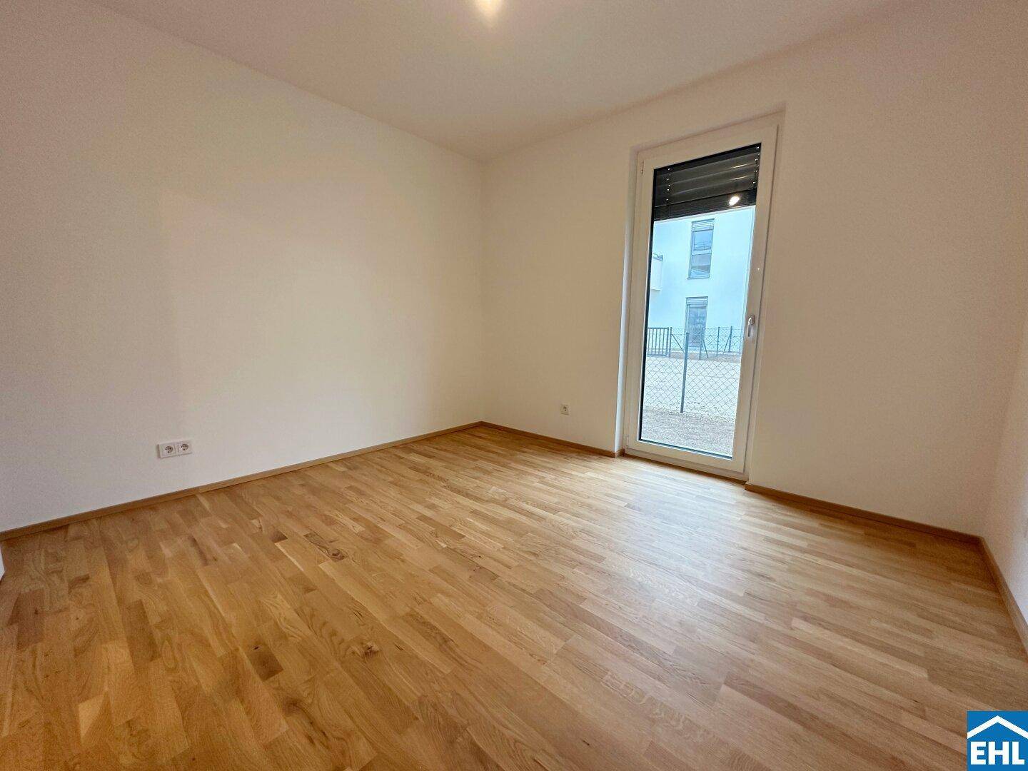 Helles, unmöbliertes Schlafzimmer mit Holzboden und Fenster, das einen Blick auf die Umgebung bietet.