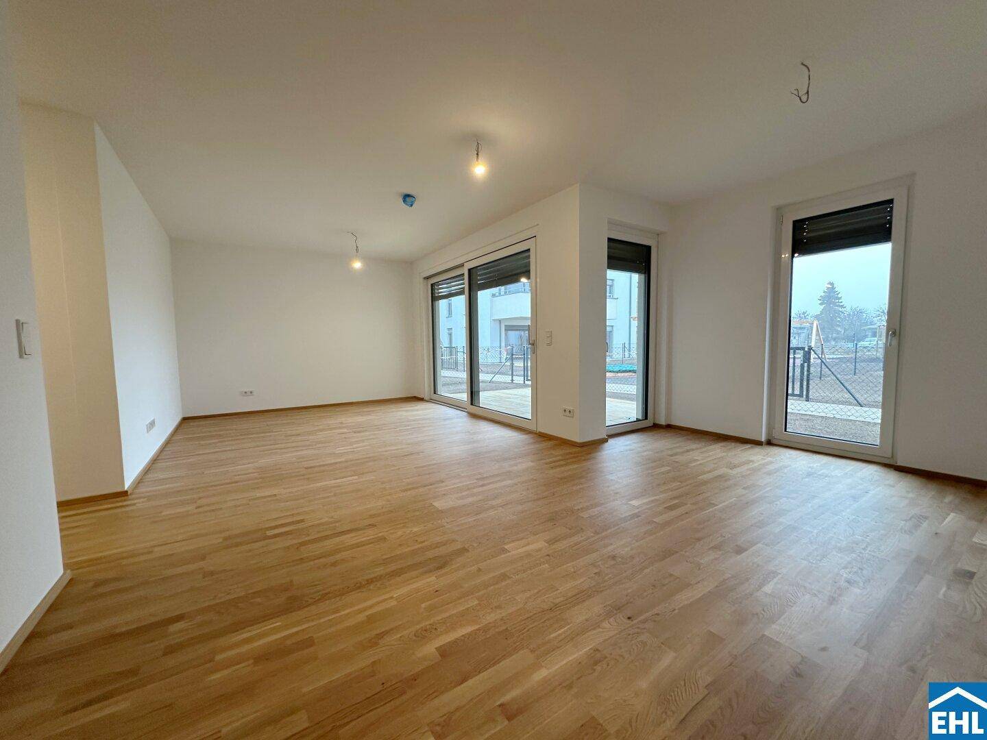 Geräumiger, leerer Wohnbereich mit hellem Holzboden und großen Fenstern, bereit zur individuellen Gestaltung.