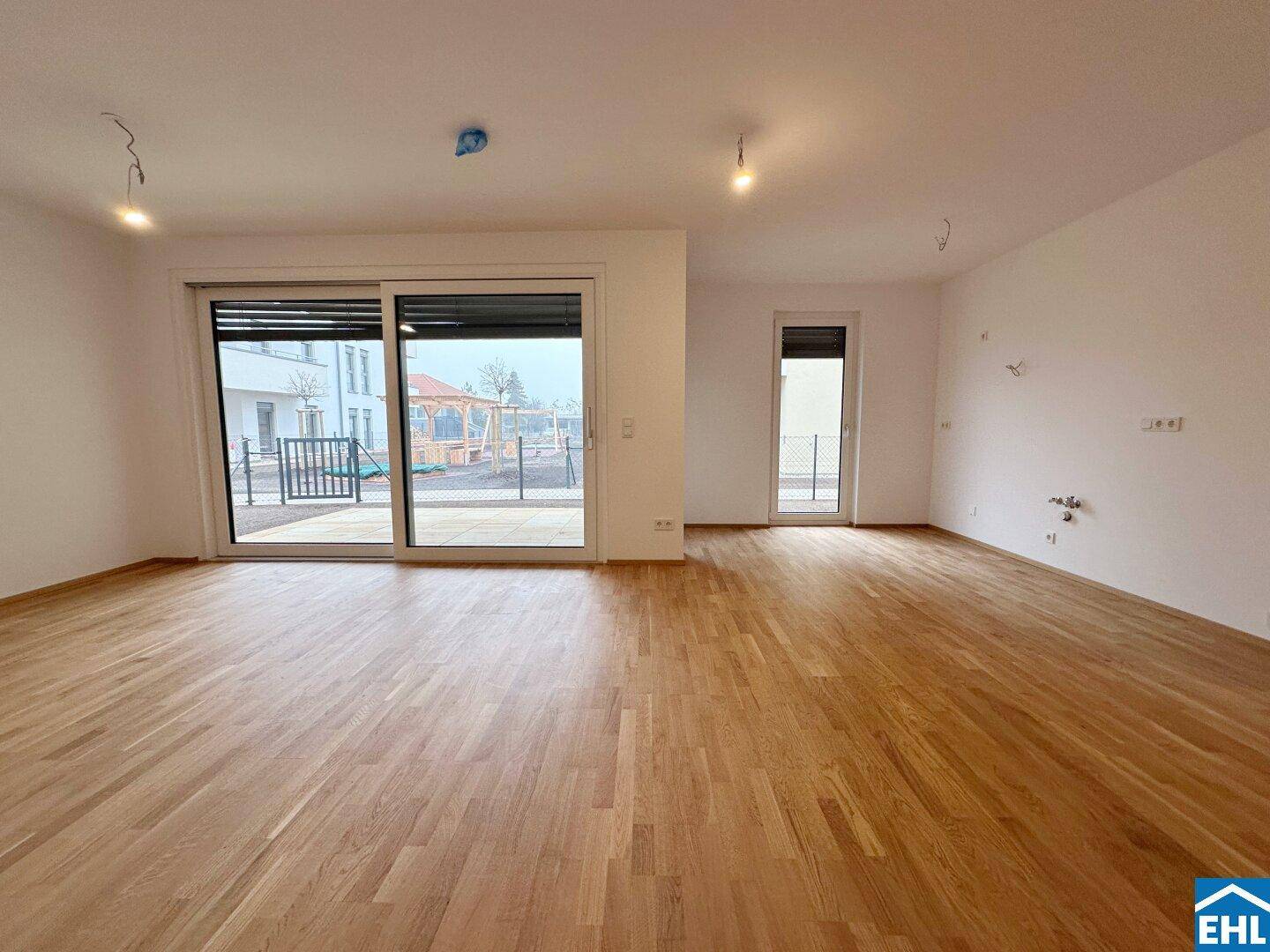 Heller Wohnbereich mit Holzboden und Schiebetüren, die viel Tageslicht hereinlassen und Zugang nach draußen bieten.