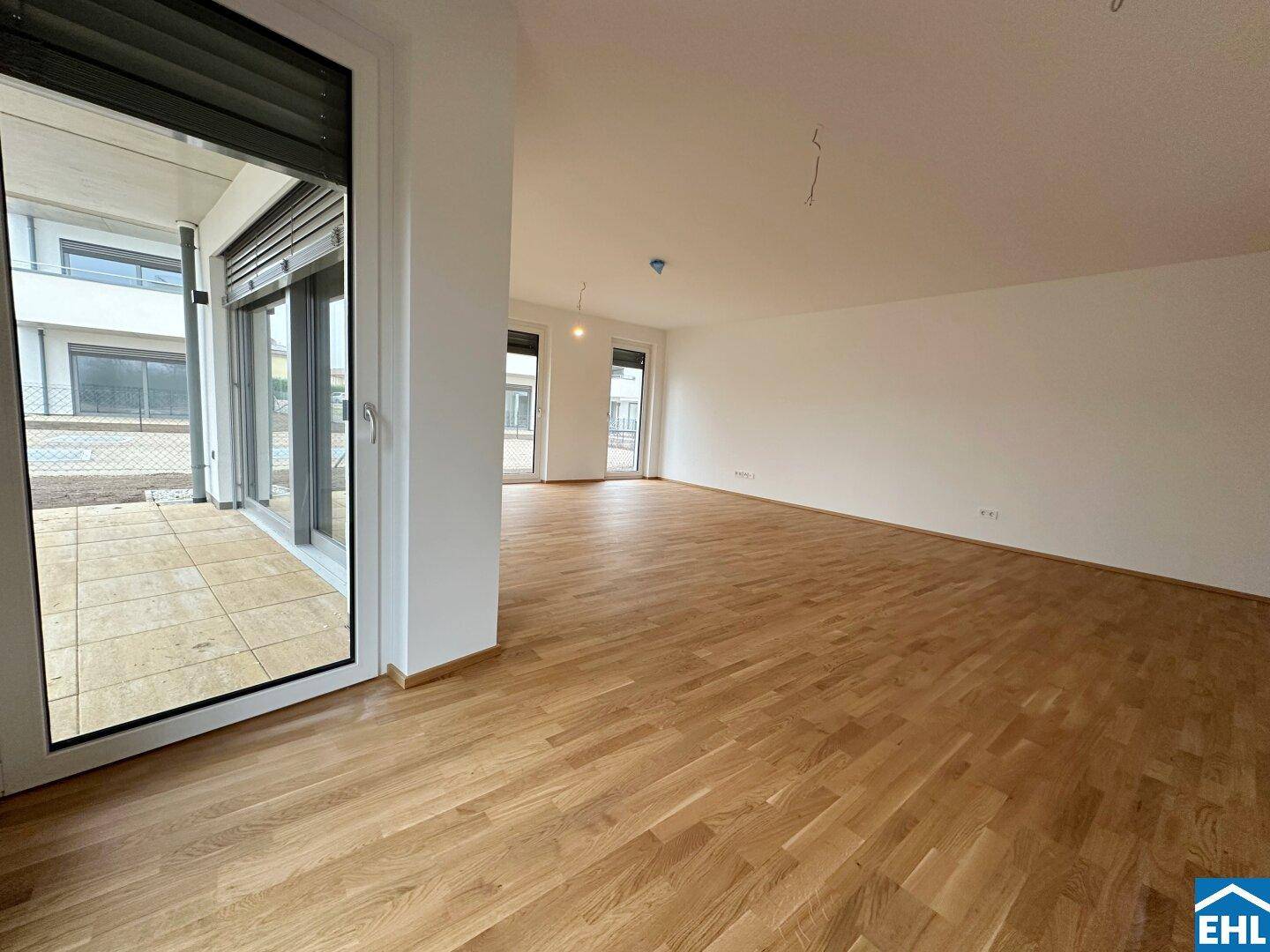 Heller Wohnbereich mit Parkettboden und breiter Schiebetür, die den Zugang zu einer Terrasse ermöglicht.