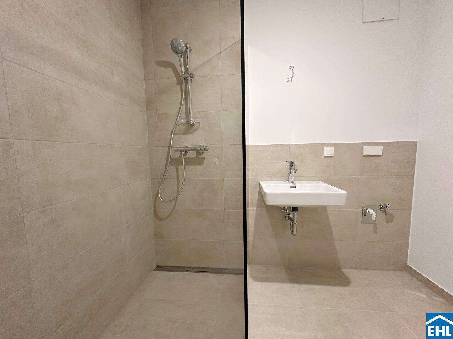 Modernes Badezimmer mit ebenerdiger Dusche und einem einzelnen Waschbecken auf hellen Fliesen.