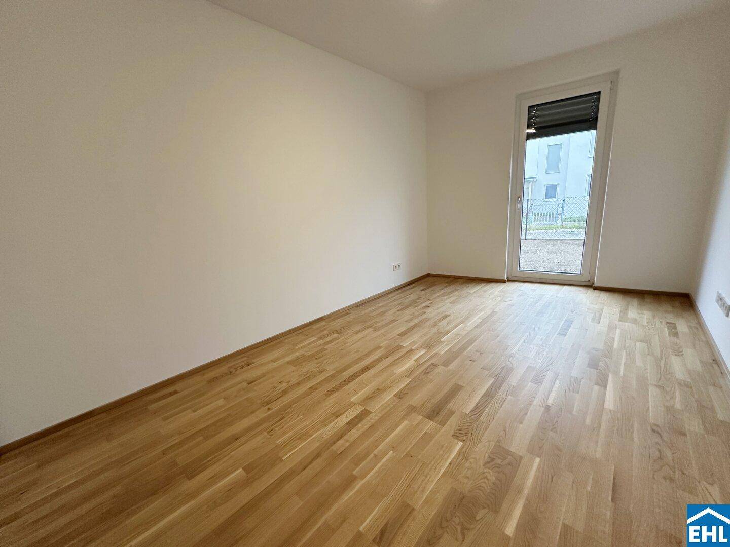 Leeres Zimmer mit hellem Parkettboden und Zugang zu einem Außenbereich durch eine große Tür.