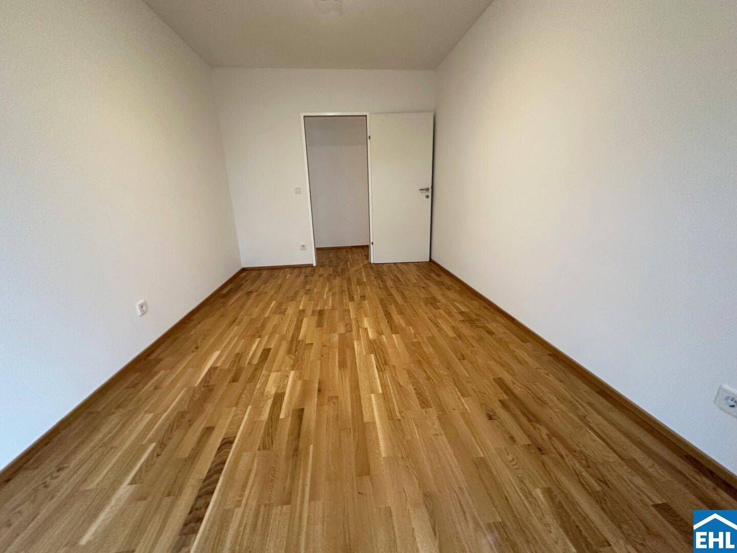 Unmöbliertes Zimmer mit hellem Parkettboden und weiß gestrichenen Wänden, bereit zur individuellen Gestaltung.