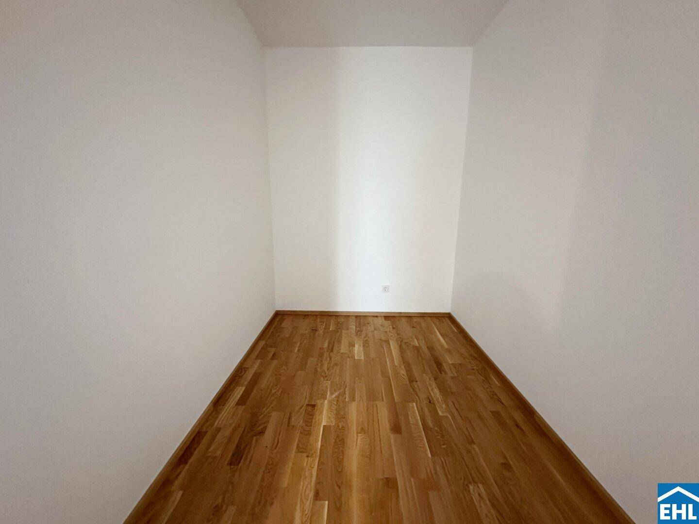 Schmaler, leerer Raum mit Parkettboden und weißen Wänden, nutzbar als Abstellraum oder begehbarer Kleiderschrank.