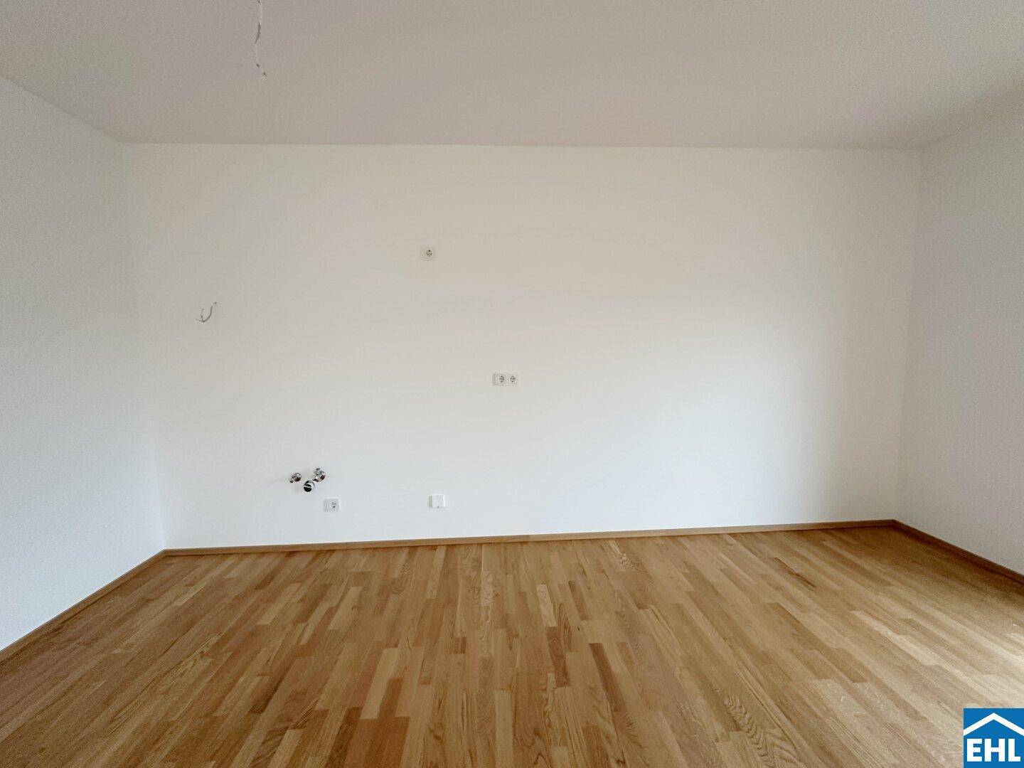 Leerer Küchenbereich mit Parkettboden und vorbereiteten Anschlüssen für eine Einbauküche.
