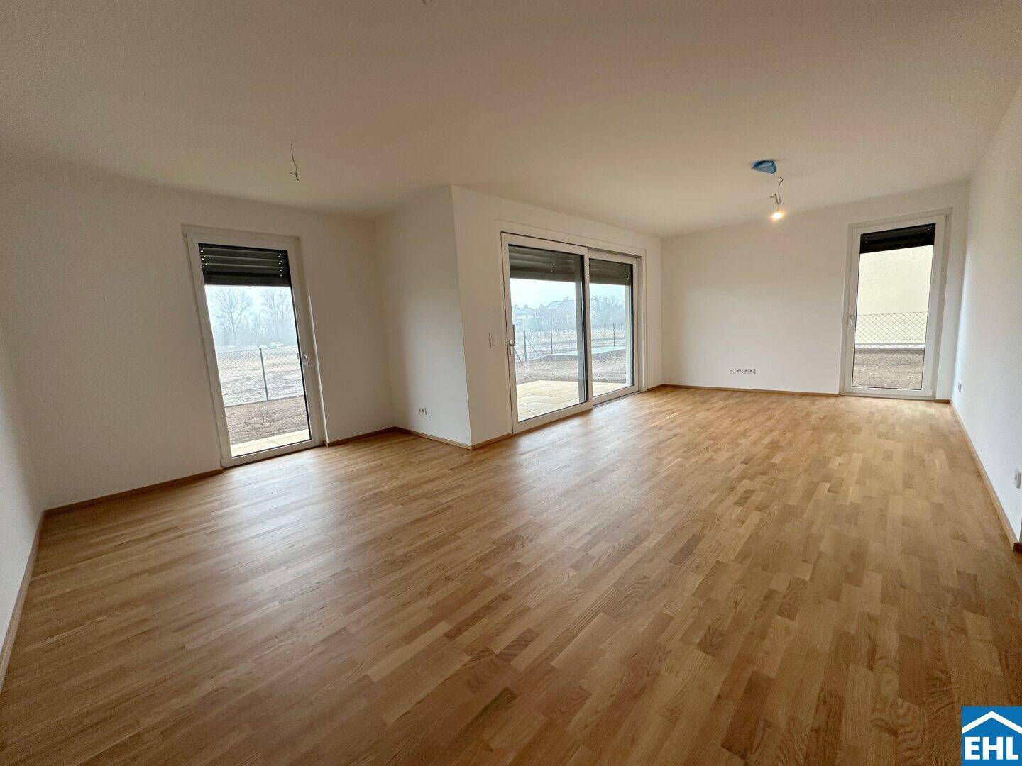 Helles Wohnzimmer mit Holzboden und großen Fenstern, die viel Tageslicht hereinlassen.