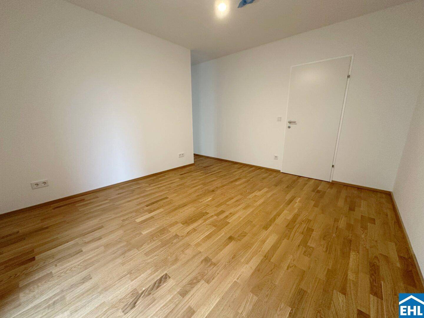 Leeres Zimmer mit Parkettboden und weißer Tür, bereit zur individuellen Gestaltung.