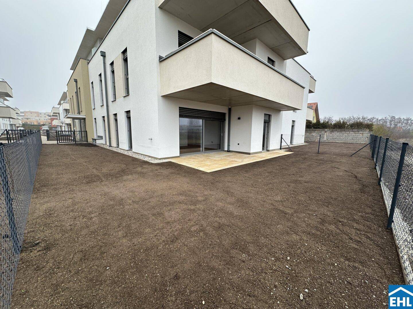 Hinterhof mit vorbereitetem Gartenbereich und kleiner Terrasse an einem modernen Gebäude.
