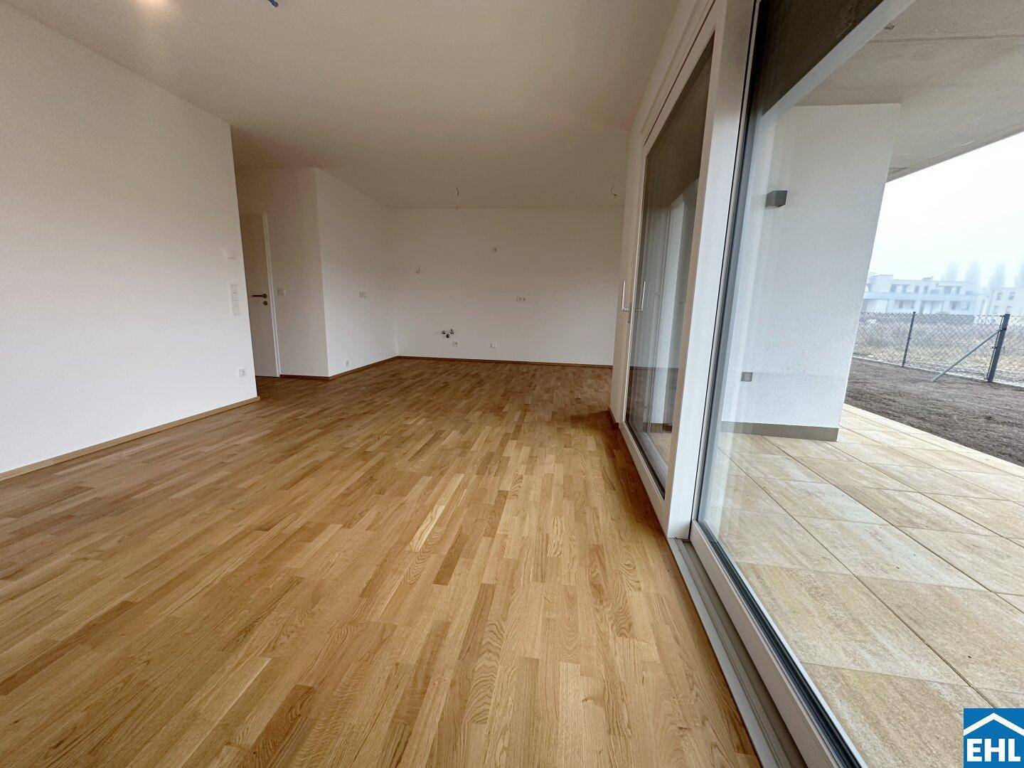 Geräumiger Wohnbereich mit Parkettboden und großem Fenster zur Terrasse.