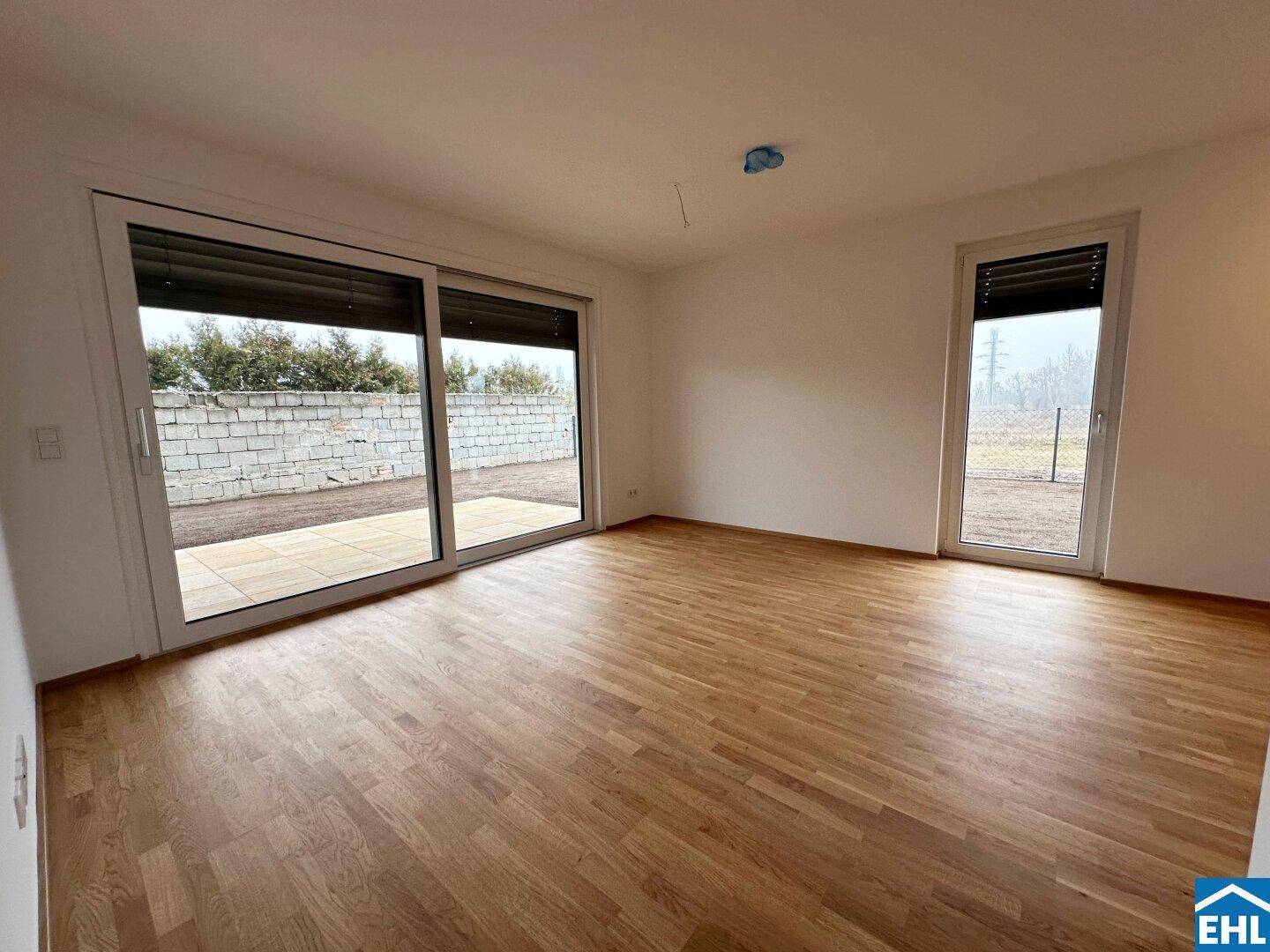 Geräumiges Wohnzimmer mit Holzboden und großen Schiebetüren, die auf eine Terrasse führen.
