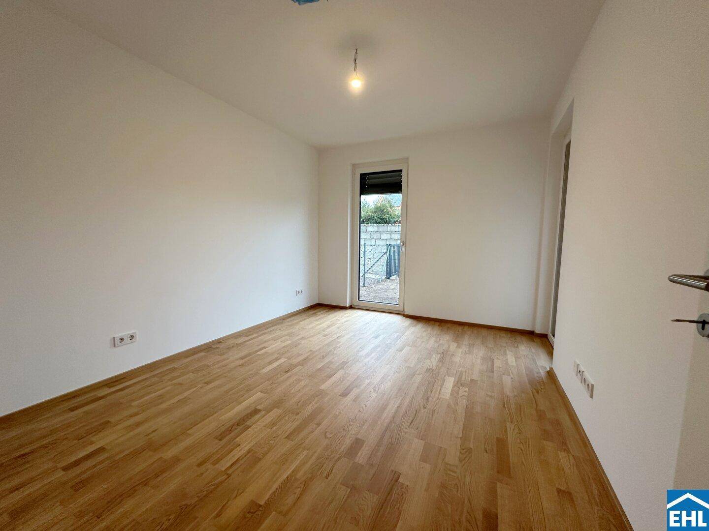 Helles Schlafzimmer mit Holzboden und einer Tür, die zu einem Außenbereich führt.