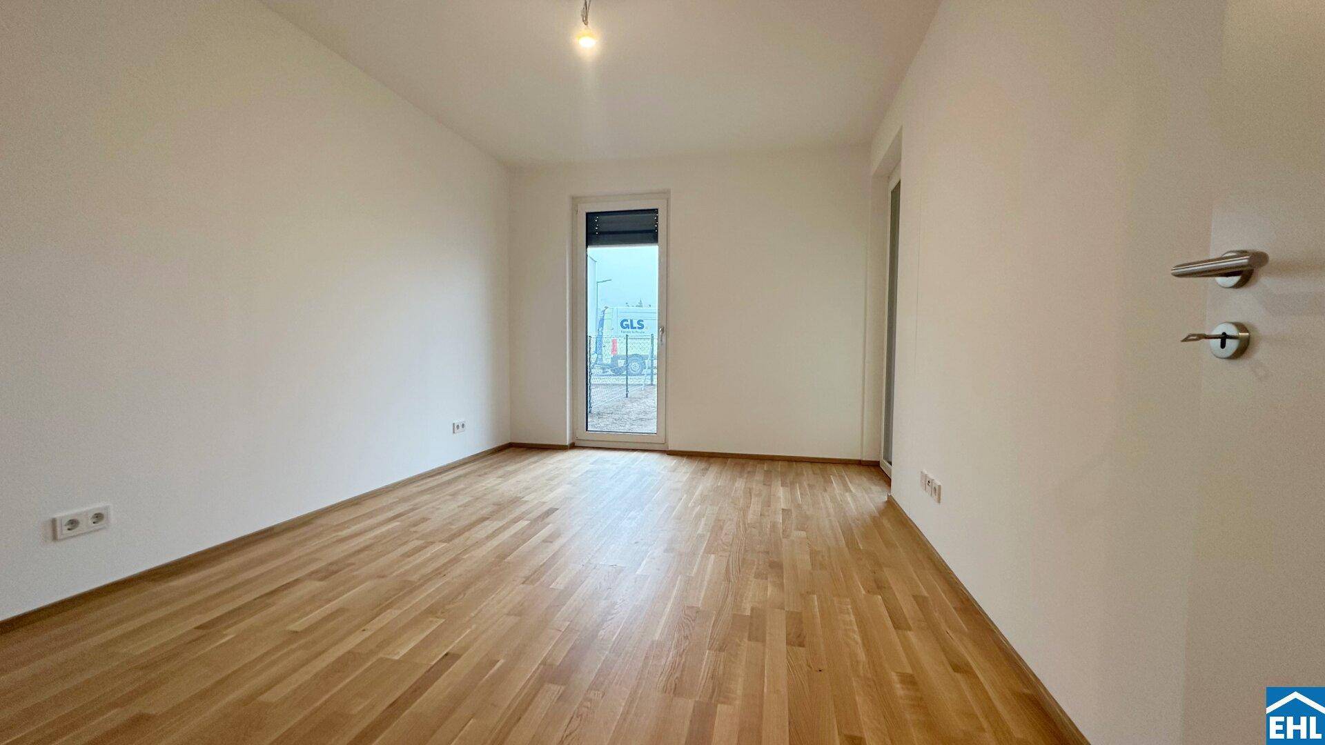 Leeres Zimmer mit hellem Holzboden und einem Fenster, das viel Tageslicht hereinlässt.