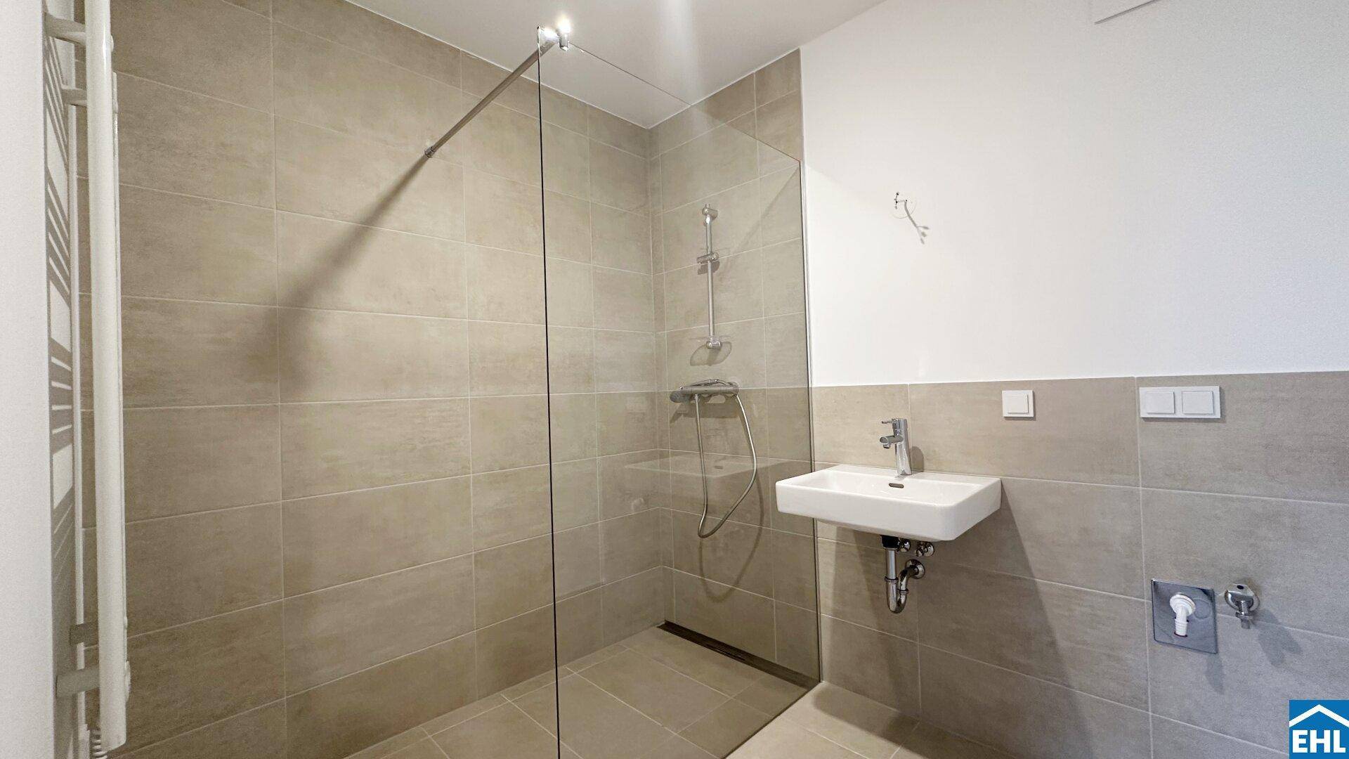 Modernes Badezimmer mit beigen Fliesen, ebenerdiger Dusche und einem einzelnen Waschbecken.