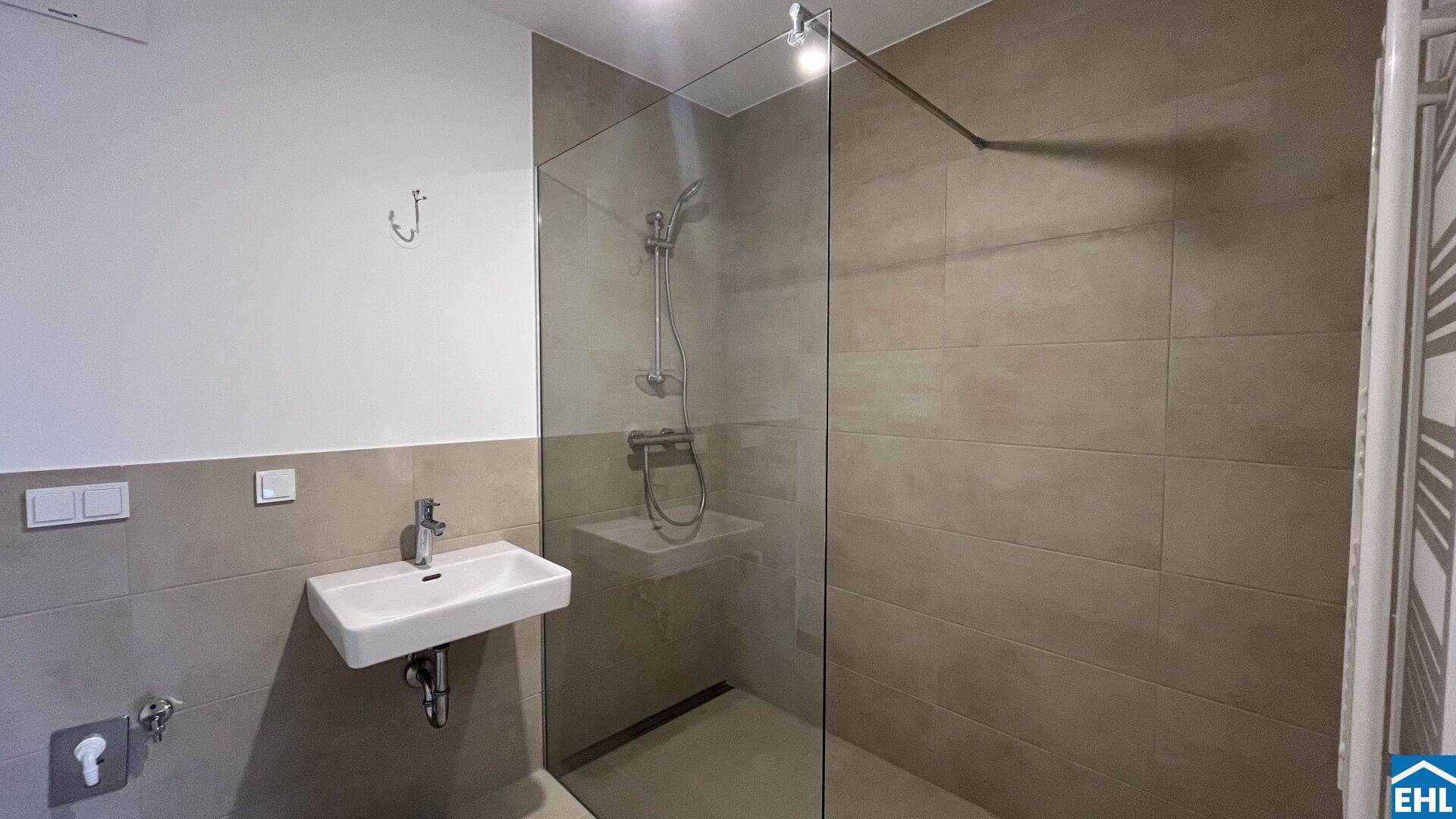 Modernes Badezimmer mit begehbarer Dusche, Einzelwaschbecken und hellen Fliesen.