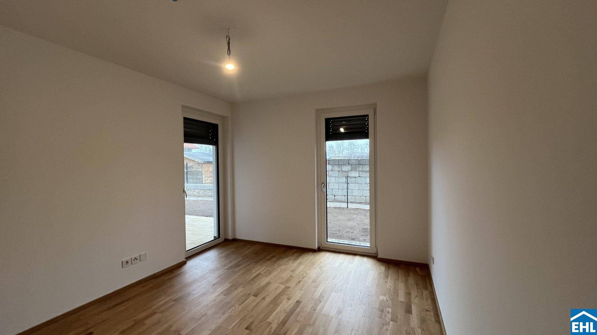 Heller, leerer Raum mit Holzboden und zwei Türen zum Außenbereich.