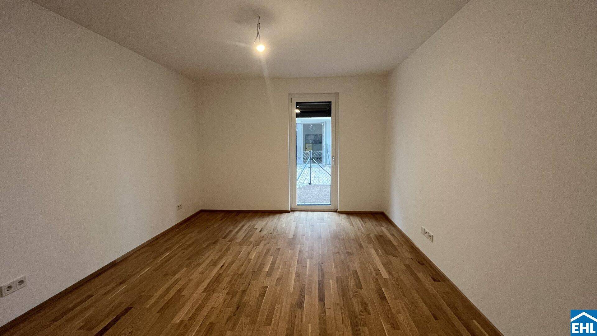 Helles, leeres Zimmer mit Parkettboden und Fenstertür zum Außenbereich.