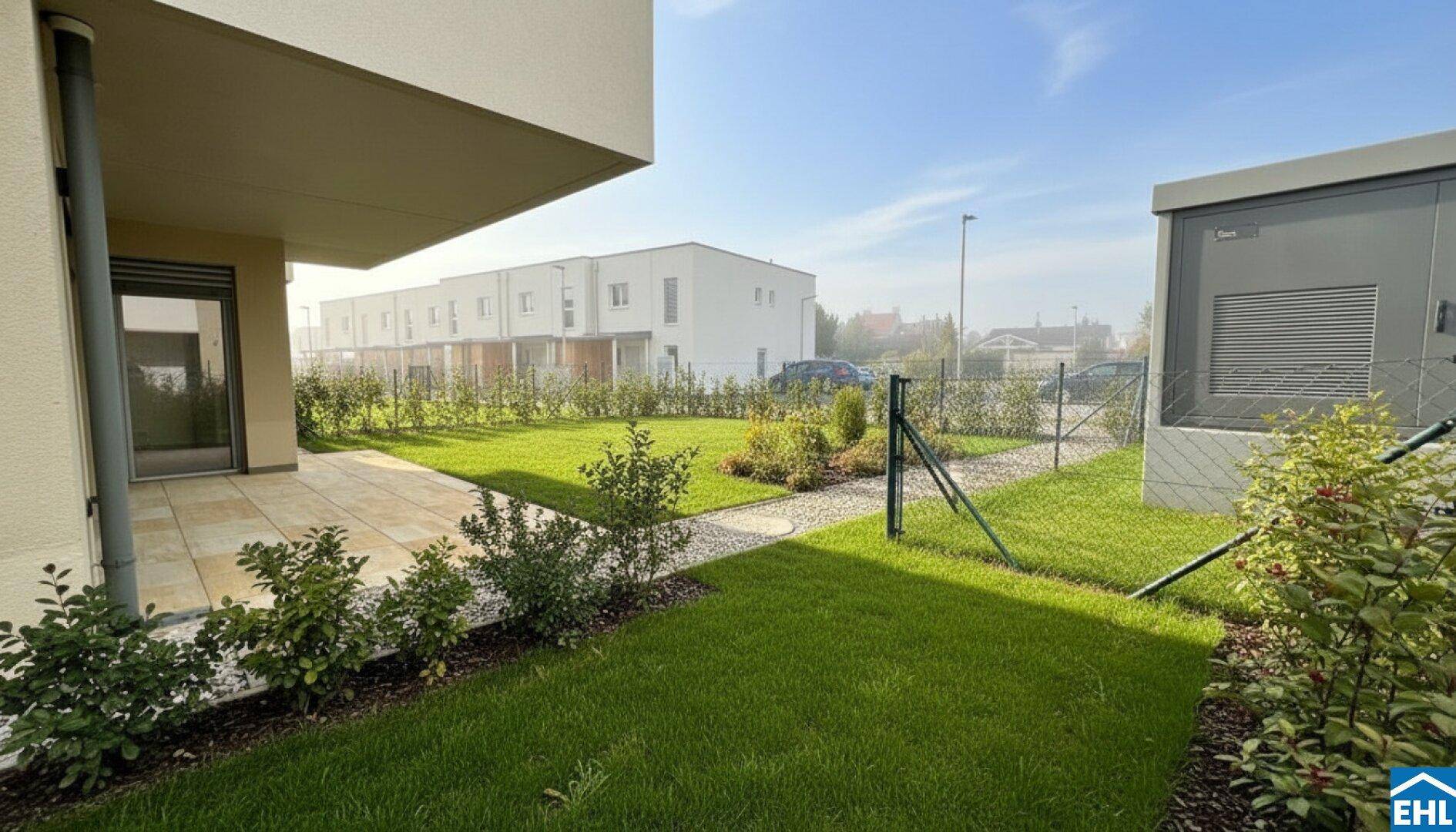 Gepflegter Gartenbereich mit Rasenfläche und einer kleinen Terrasse neben dem modernen Gebäude.