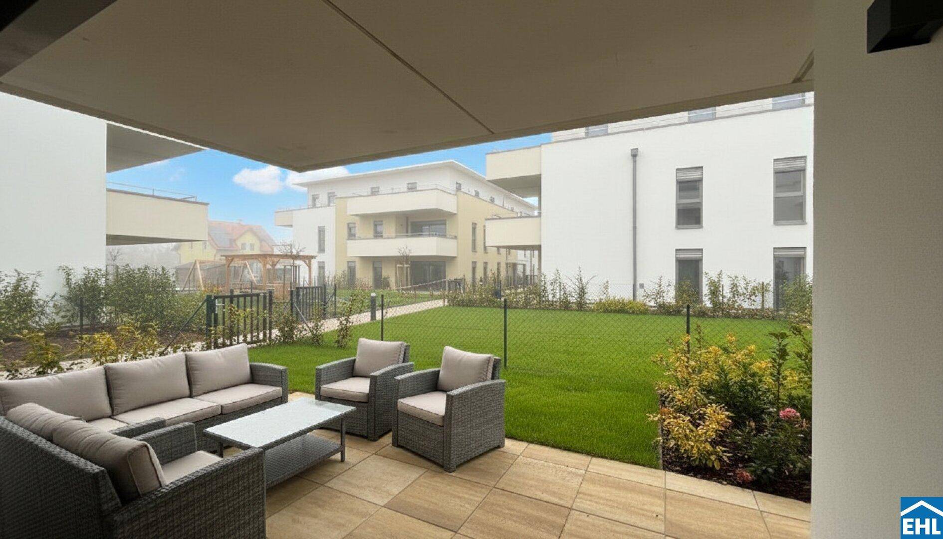 Möblierte Terrasse mit Rasenfläche und Blick auf die moderne Wohnanlage.